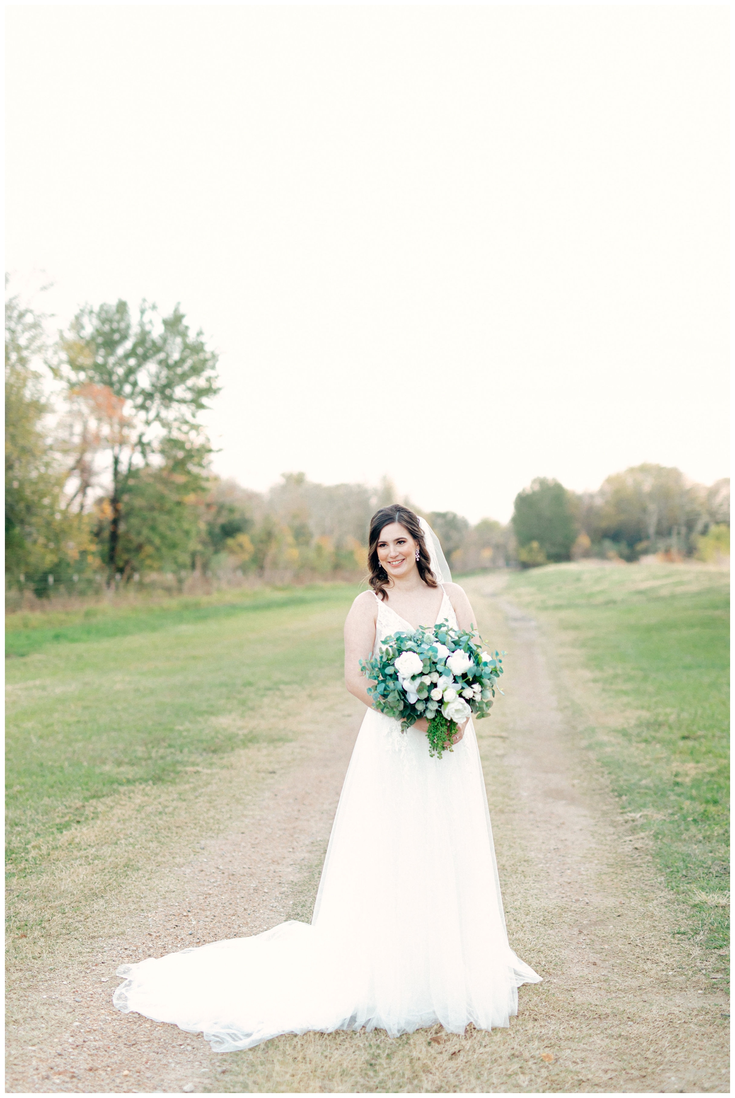 bride holding white floral bouquet standing on pathway outside at Beckendorff Farms wedding