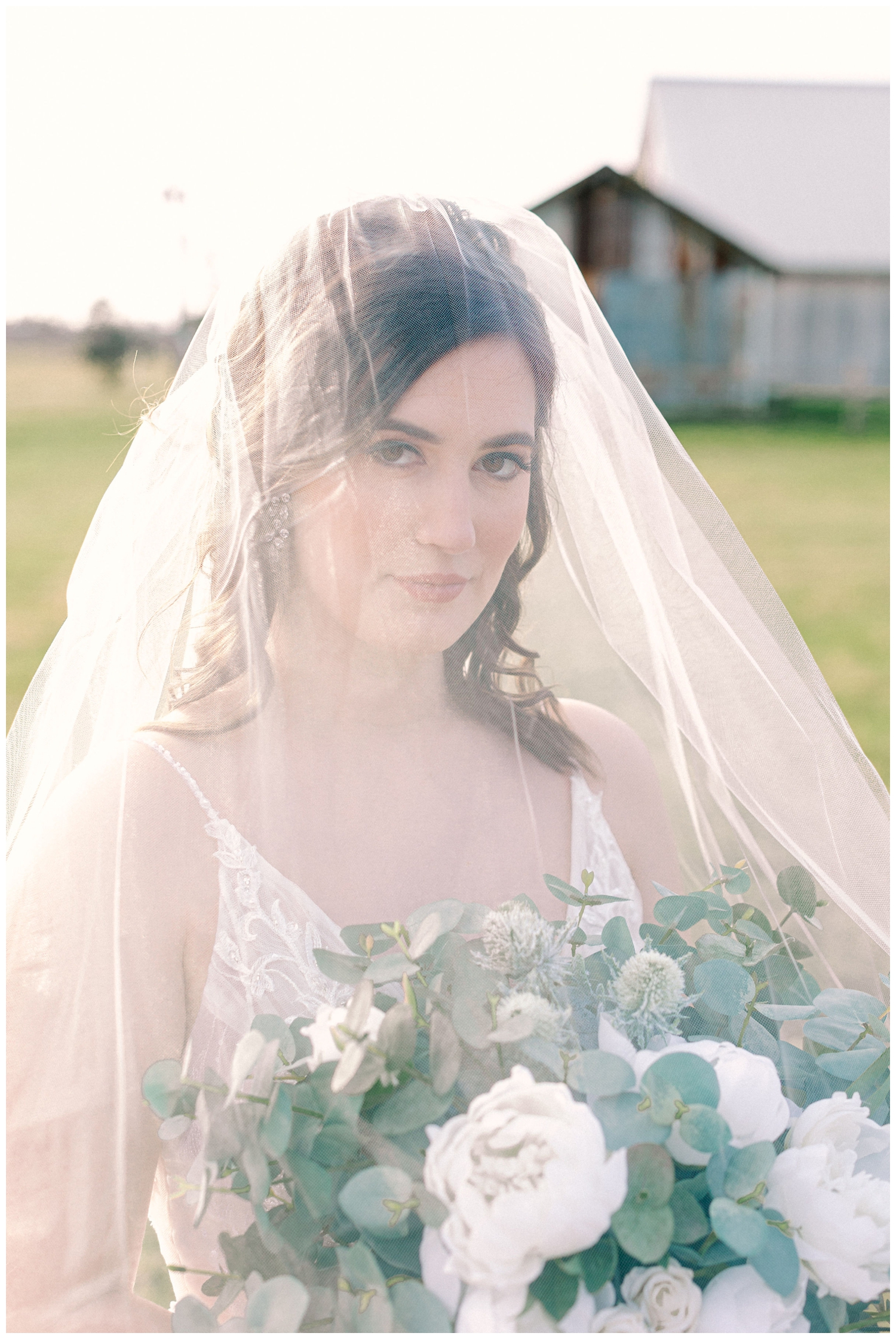 bride with veil over her head holding white floral bouquet on lawn at Beckendorff Farms wedding