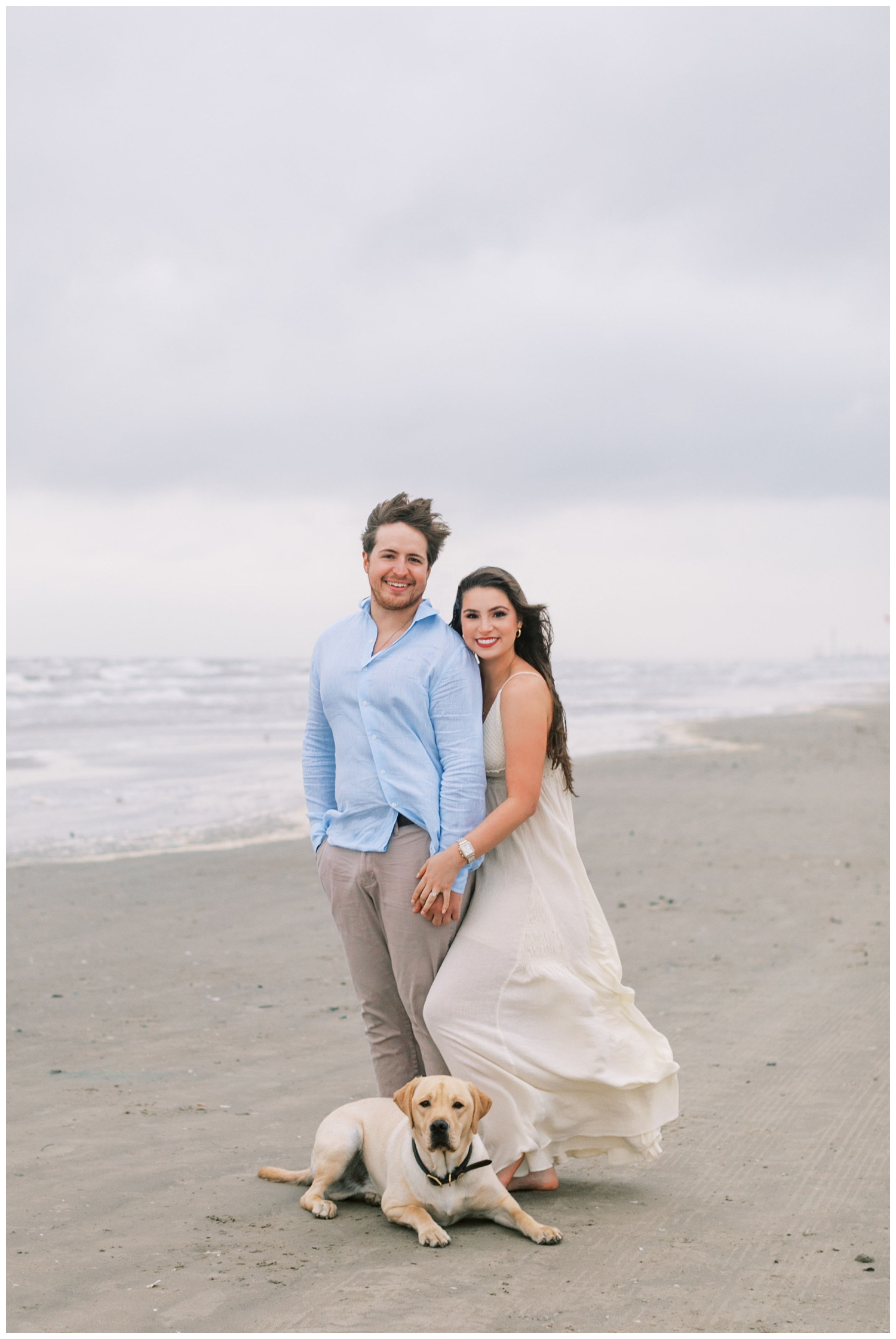 couple standing on Galveston beach in white dress, khakis and with a dog
