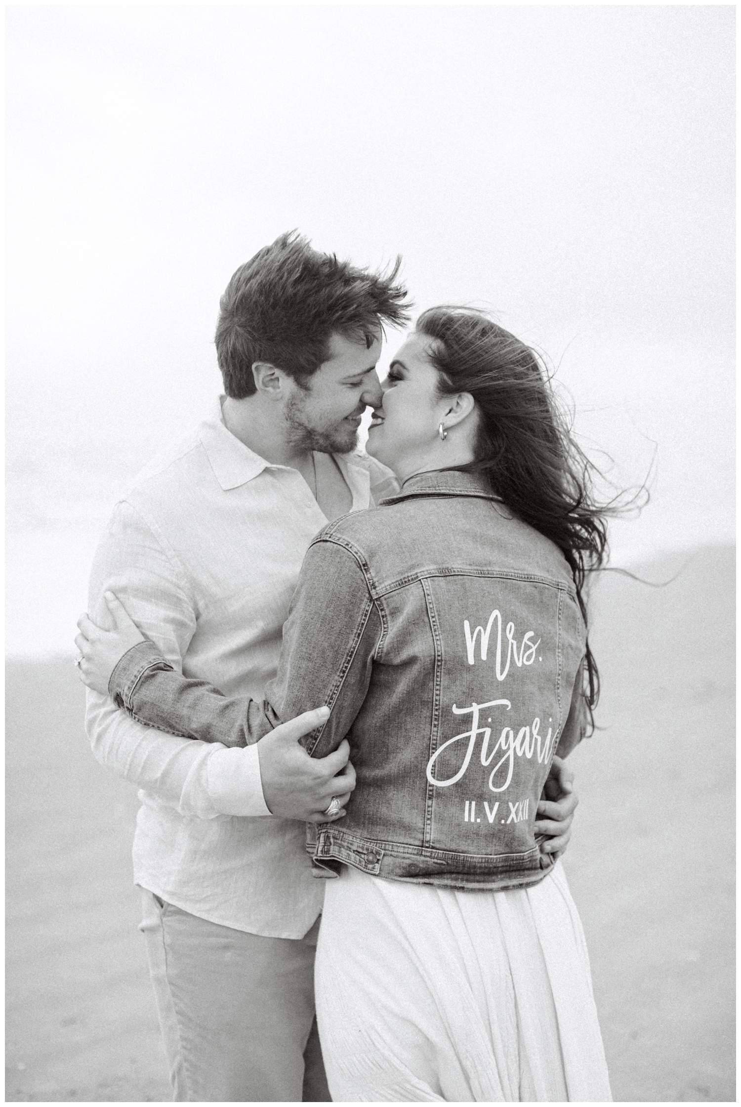 black and white portrait of couple kissing with bride wearing monogrammed denim jacket at Galveston engagement session