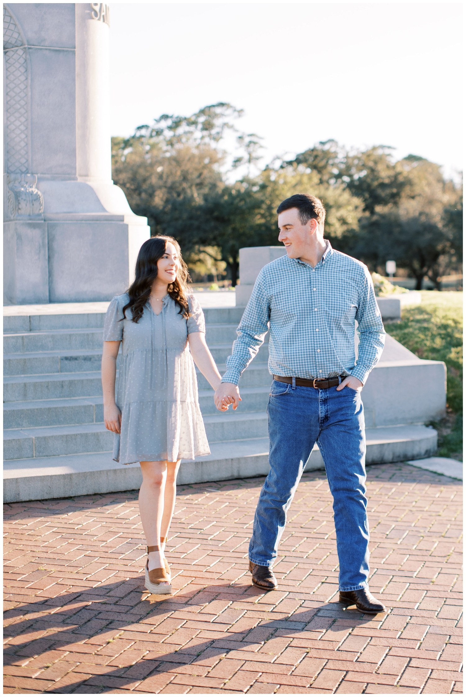 Houston engagement session with couple holding hands and walking in front of monument at Hermann Park in Houston, Texas