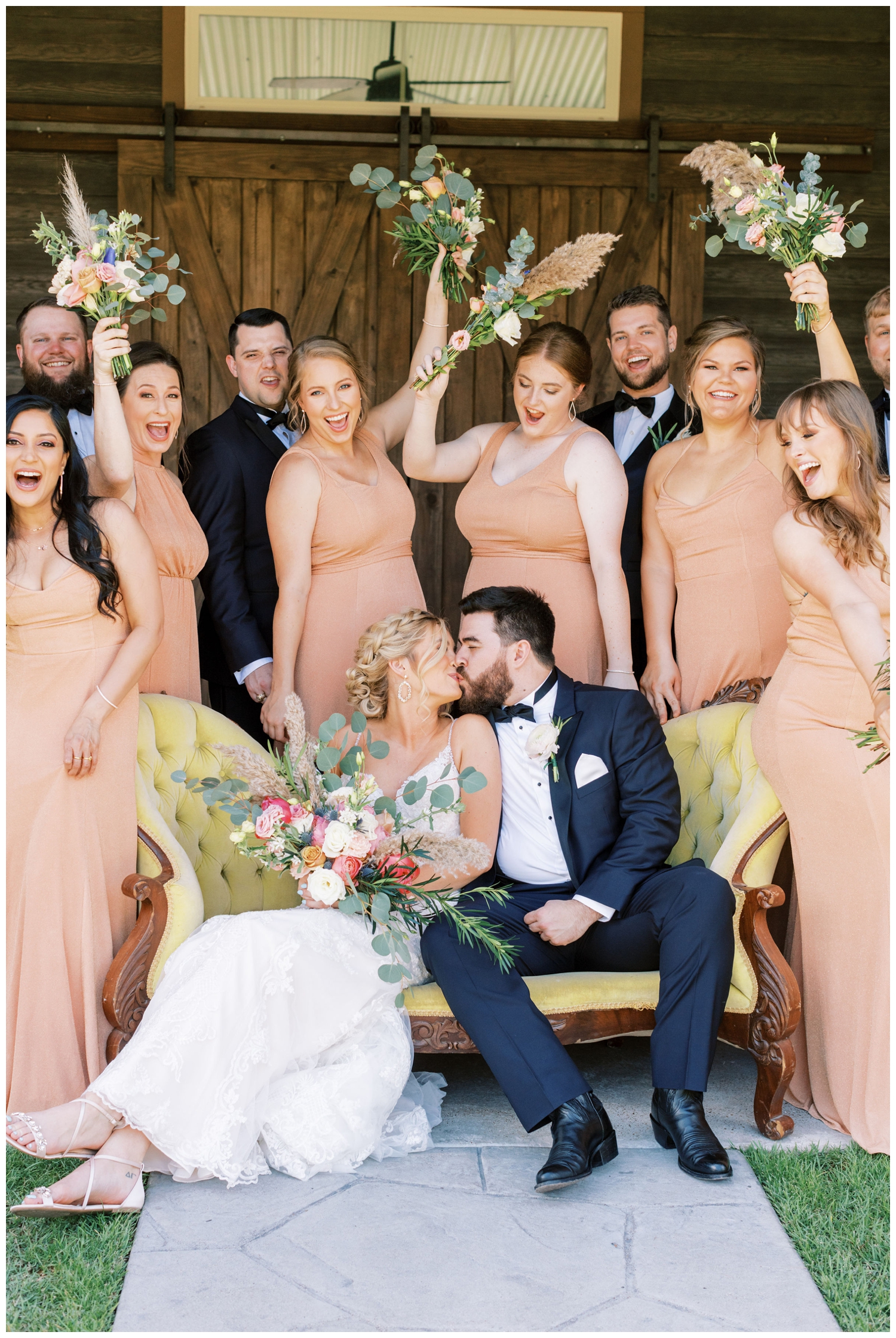 bride and groom kissing surrounded by their wedding party and sitting on a yellow couch at Peach Creek Ranch Wedding venue