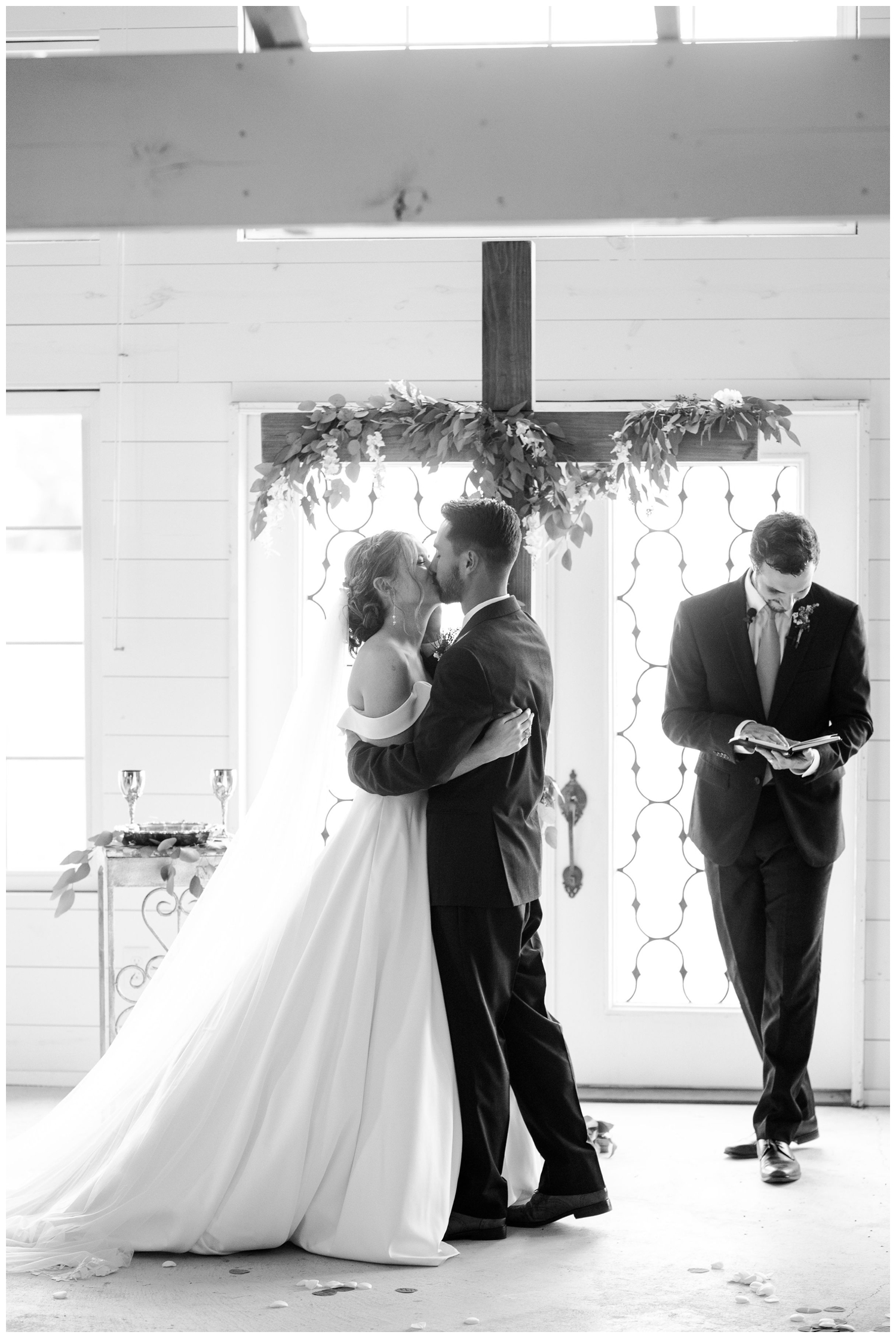 black and white photo of bride and groom kissing during ceremony at Houston white barn wedding chapel