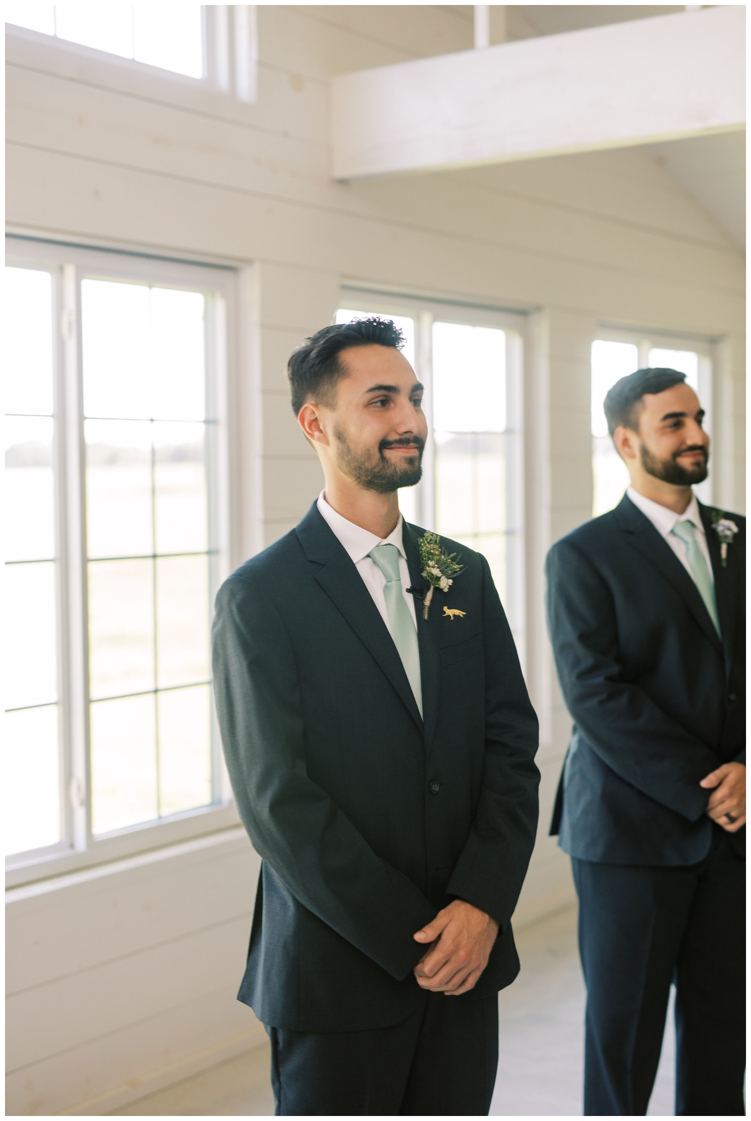 groom smiling as bride enters the white barn chapel