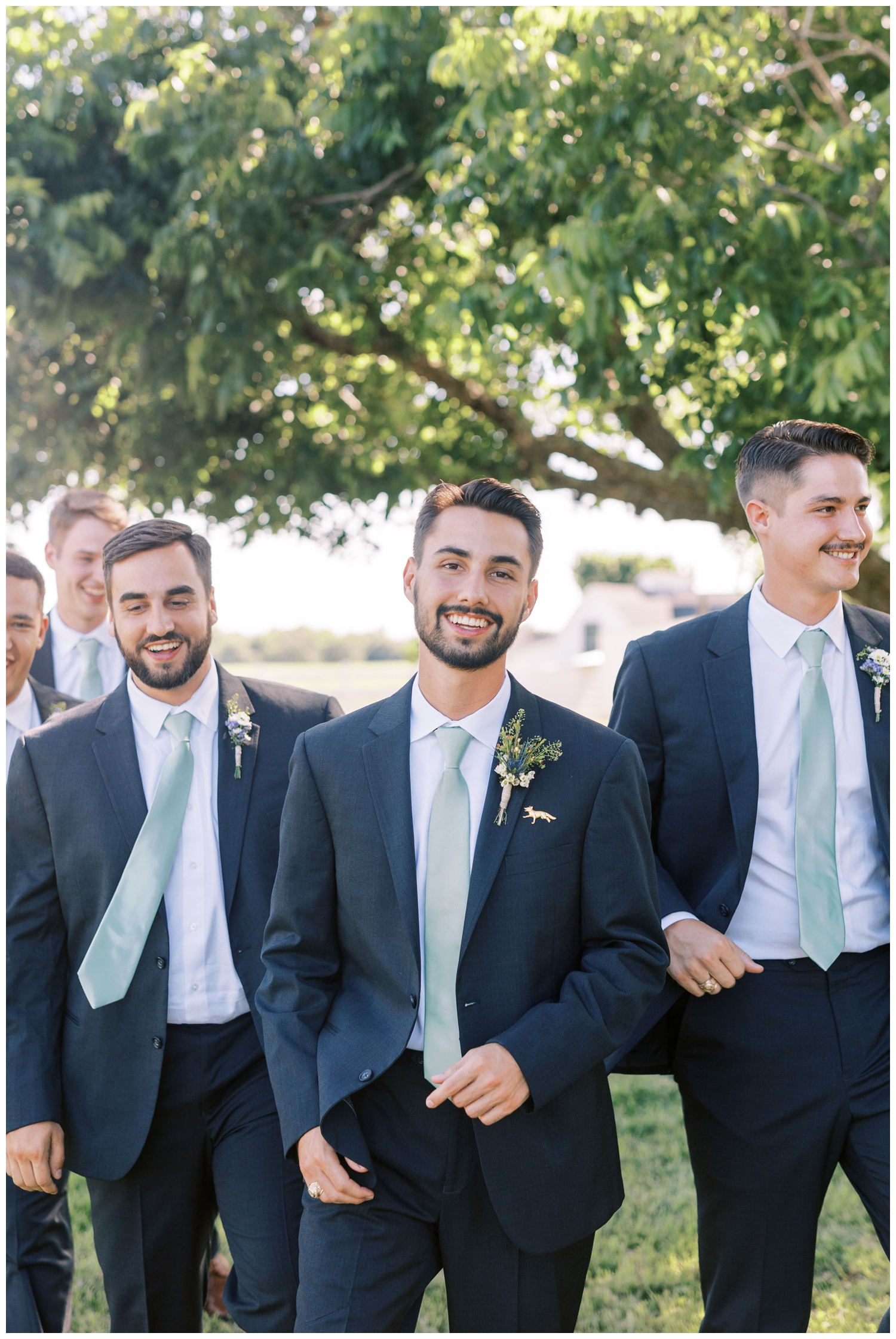 groom smiling and walking under tree at Houston white barn wedding venue