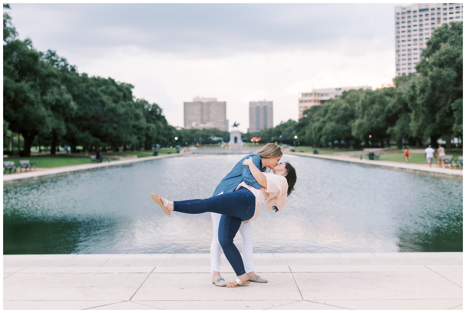 same sex couple doing dip pose in front of water at Houston engagement session