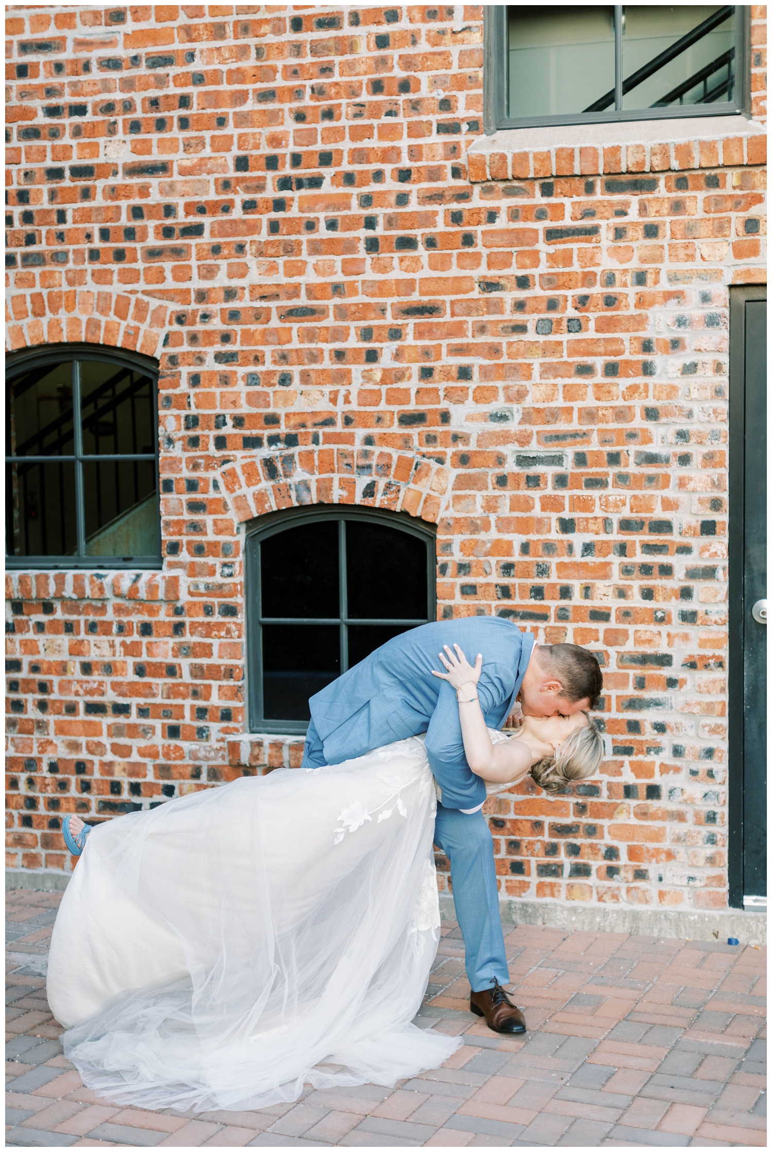 groom dipping his bride for a kiss in front on brick wall before The Annex Wedding venue portrait session
