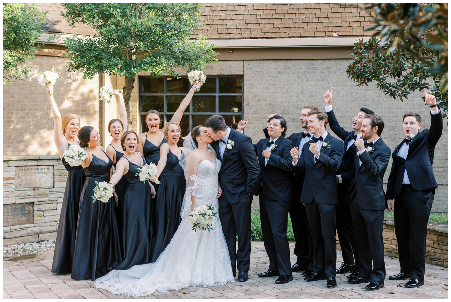bridal party in all black attire surround kissing newlyweds at Houston Junior League wedding