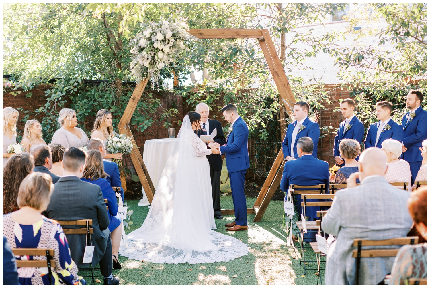 floral arch with bride and groom during groom in blue tux portrait standing under tree for Austin outdoor wedding ceremony