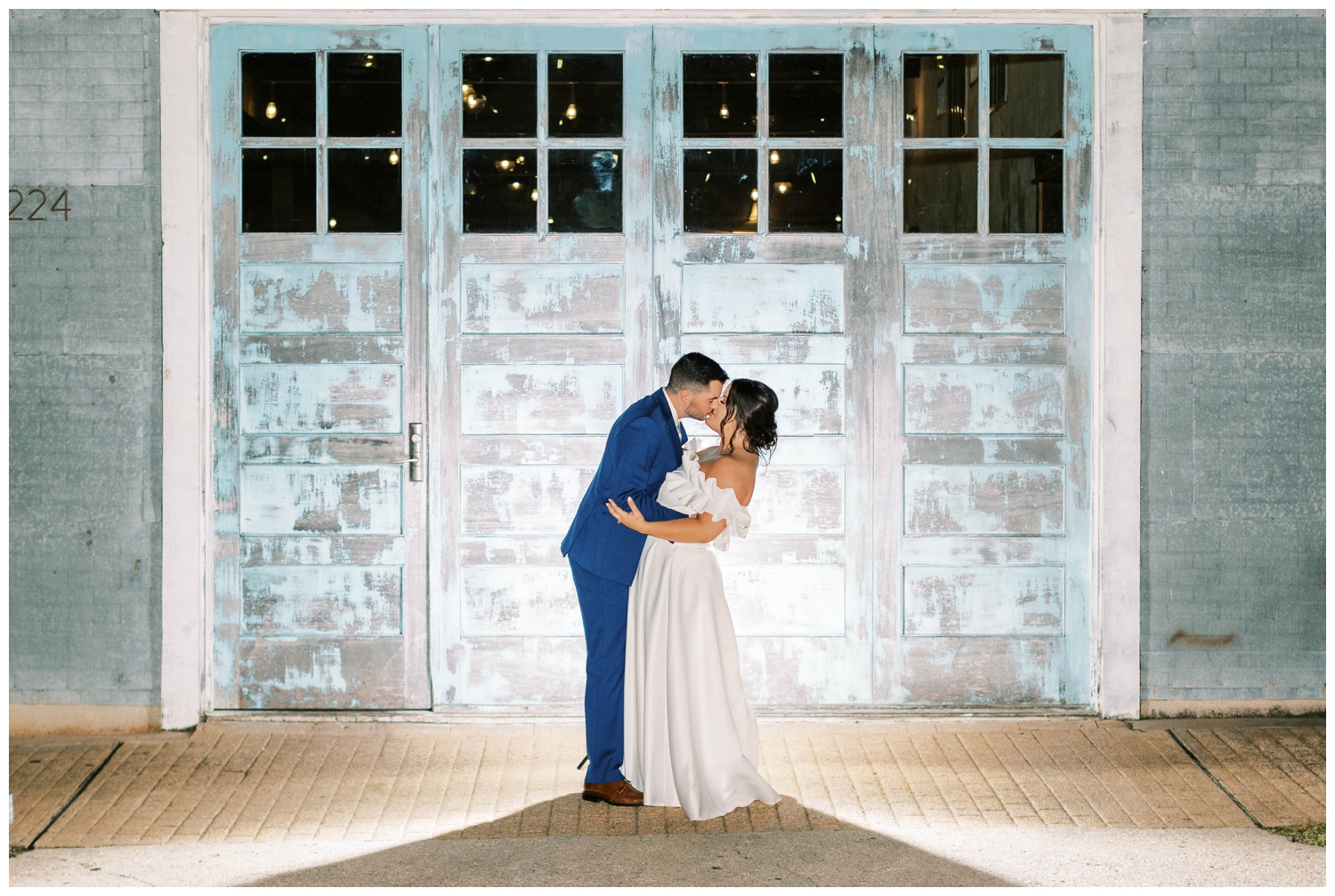 bride and groom kissing during night time portrait in front of brick wall