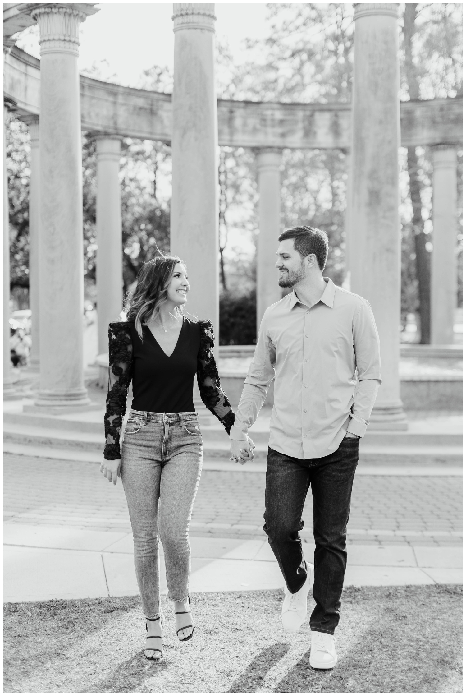 black and white image of engaged couple holding hands walking Hermann park fountain