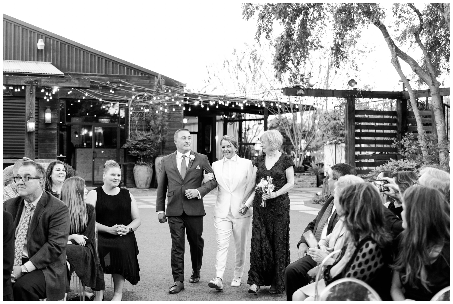 black and white image bride in white tux walking down the ceremony aisle