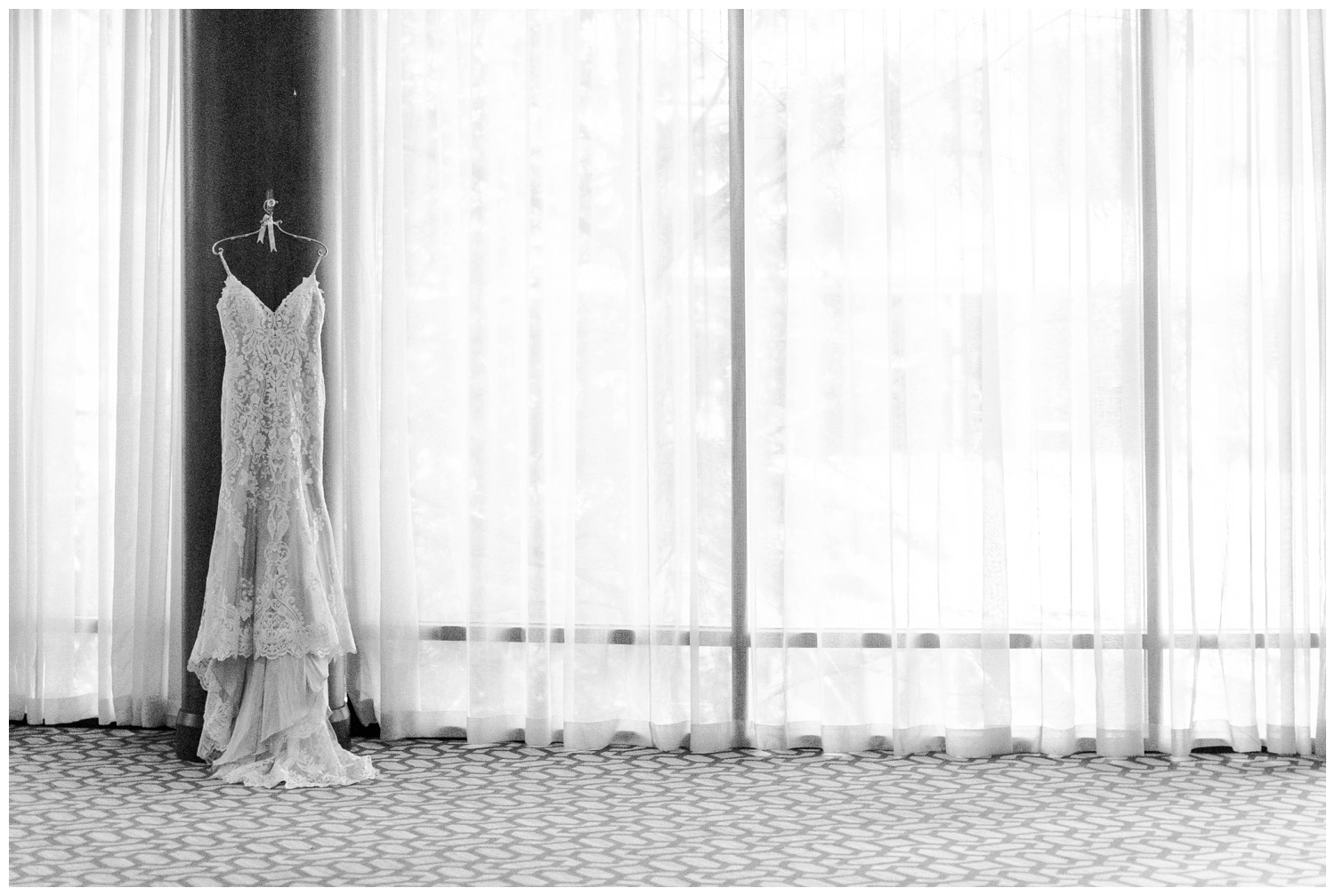 black and white image of bridal gown hanging from window at Hughes Manor