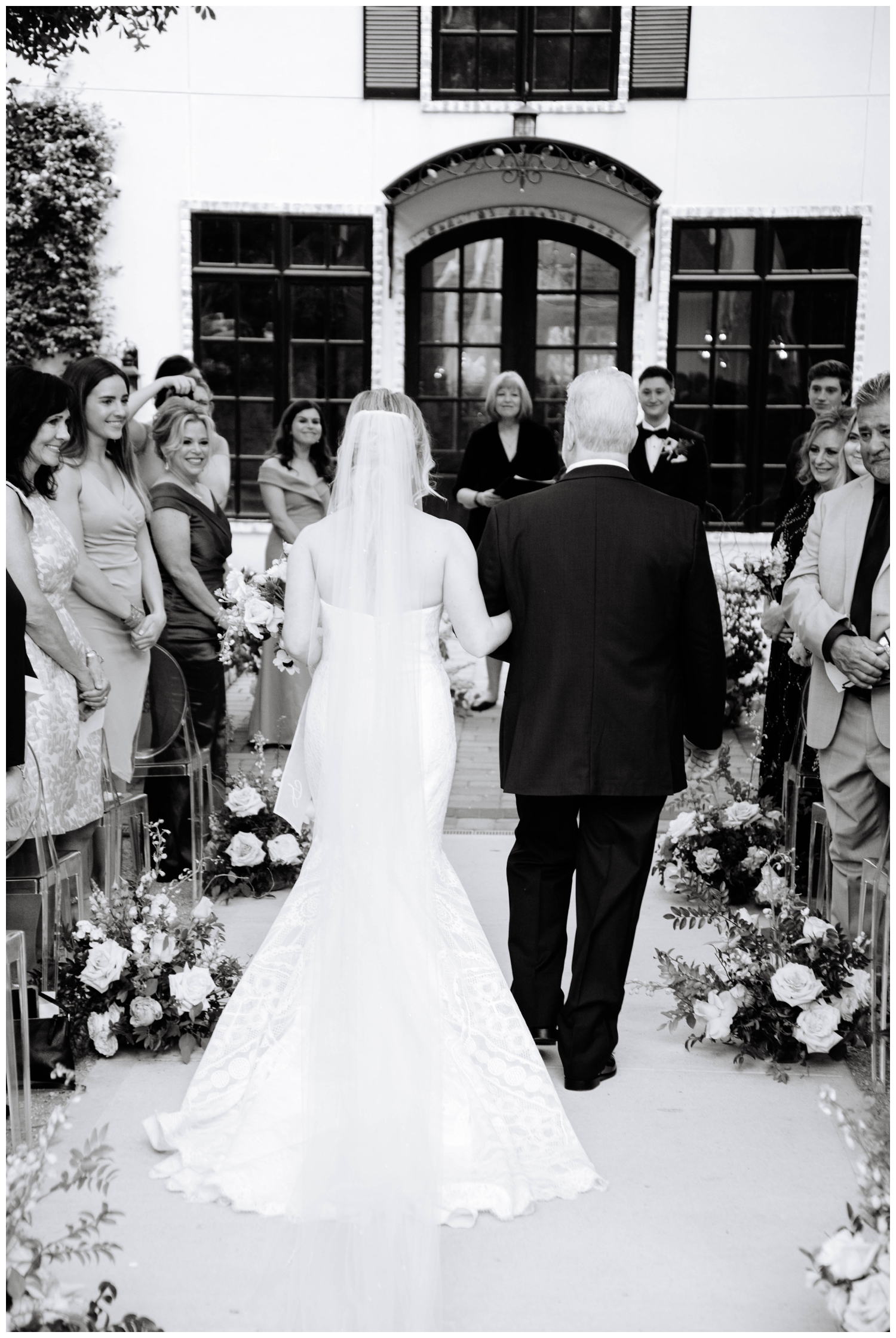 black and white portrait from behind of Dad walking bride down outdoor ceremony aisle at The Peach Orchard Wedding Venue