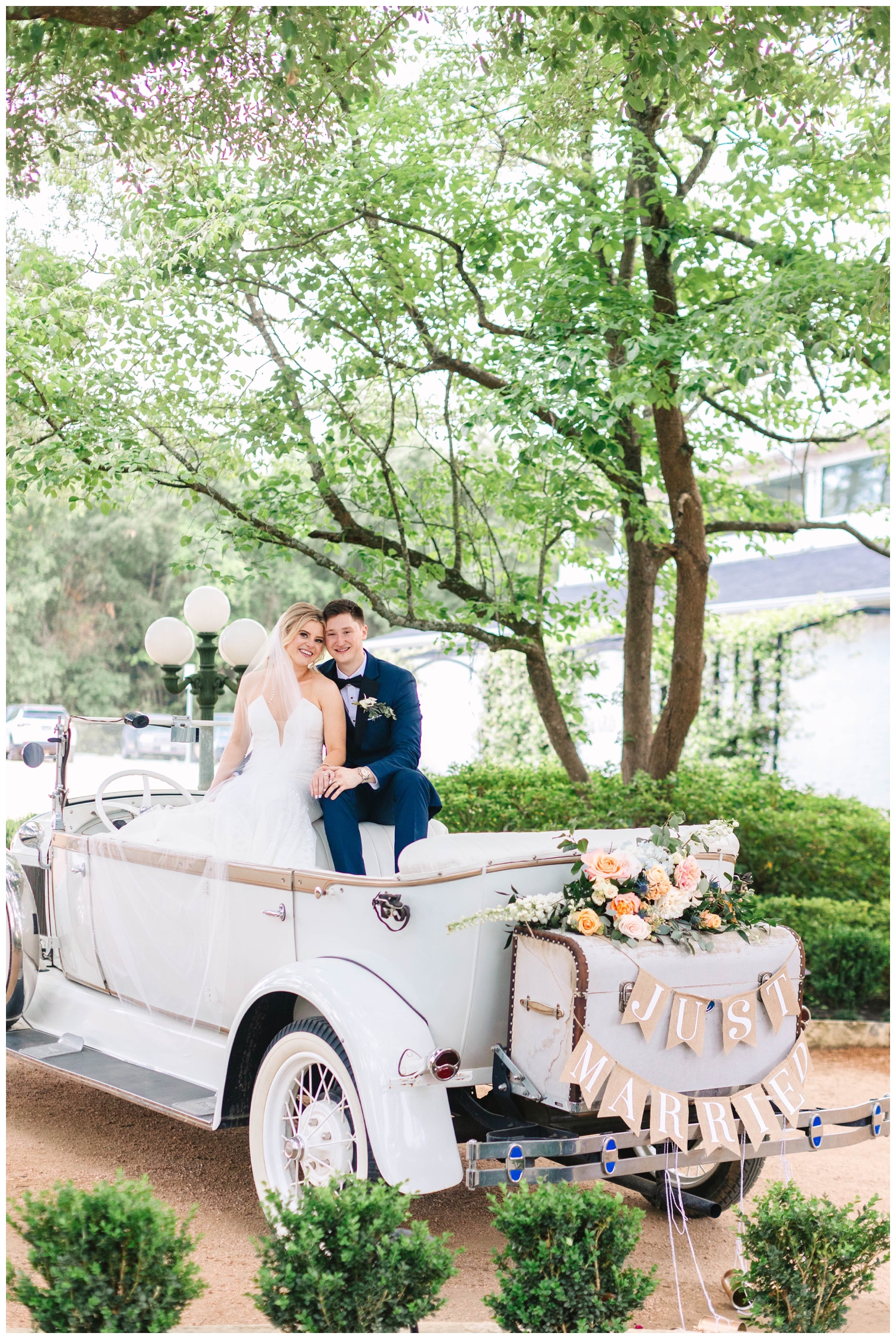 bride and groom in vintage get away car with just married sign at The Peach Orchard Beloved Ballroom Reception Talk about a reception fit for a princess! The Peach Grand Ballroom was stunning! Decor by Dulce paired the perfect toile napkins with white and gold chargers, dusty blue linens, smoke colored glasses, and gold flatware. Cakes by Paula created a beautiful four tiered cake with pearl detail that looked gorgeous nestled in flowers beneath one of the stunning chandeliers inside The Peach Orchard's Beloved Ballroom. Christen and John brought in other details that reflected who they are as a couple. They set up a legacy display on a beautiful antique chest with old wedding photos of the generations that came before them on both sides. They wanted to remember the family that came before them and who helped them get to where they are today especially, if they couldn't be there with them on their special day. After the toasts were made and dinner was served, guests danced the night away! Before leaving their reception, the couple shared a private last dance. It was just the two of them in the ballroom listening to a song that was really meaningful and emotional. Christen shared, “ It was probably the first moment that we took a breath and went "Oh wow, we're married!" Christen and John exited the reception through streamers with all their family and friends cheering them on. The Peach Orchard’s 1920s vintage car named Henry drove them away as they started their new life together.