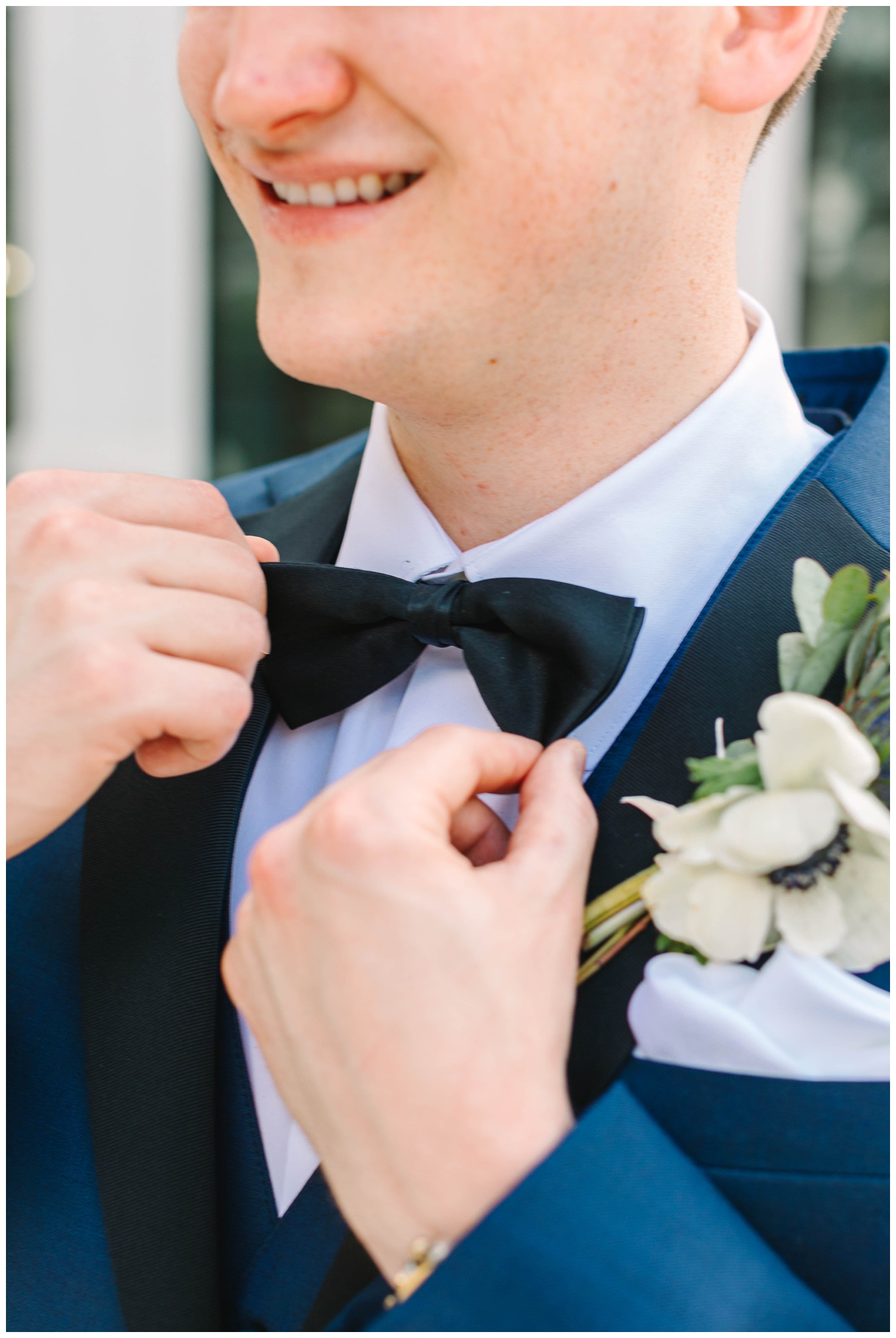groom touching bow tie in a blue suit outside The Peach Orchard wedding venue