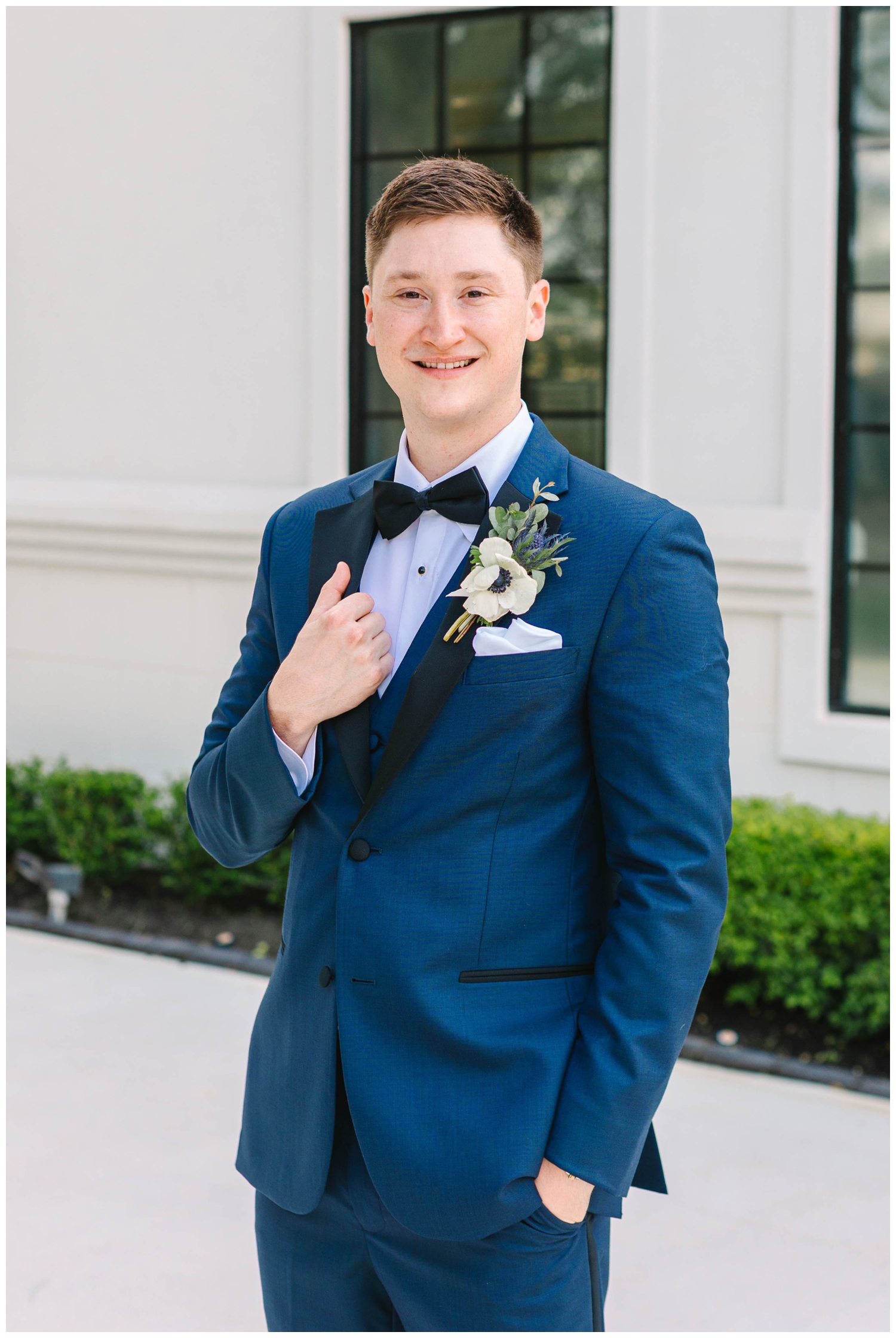the groom smiling with hand on blue jacket and black bow tie
