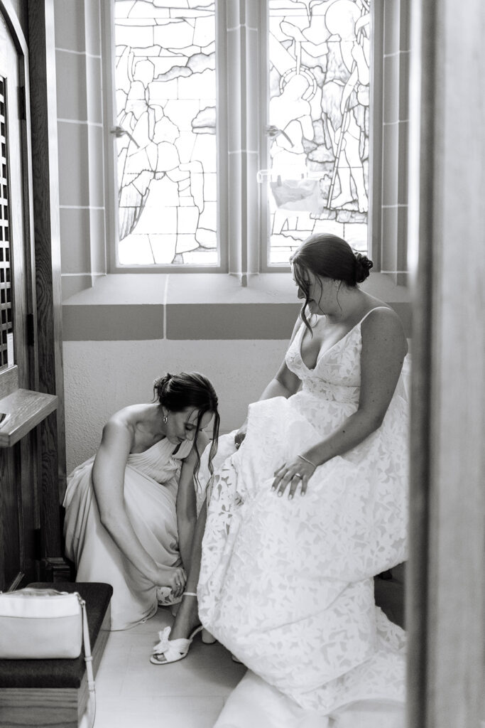Bride getting her shoes put on by bridesmaid 