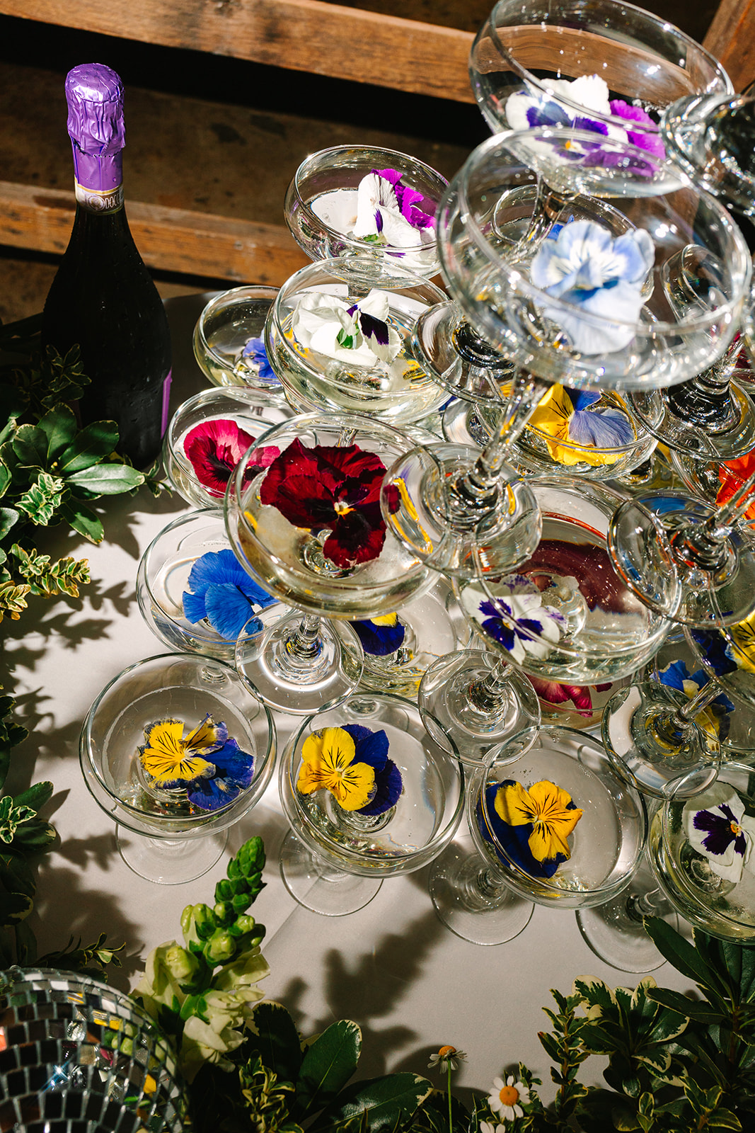 A champagne glass tower surrounded by colorful flowers and a small disco ball centerpiece on a decorated table.