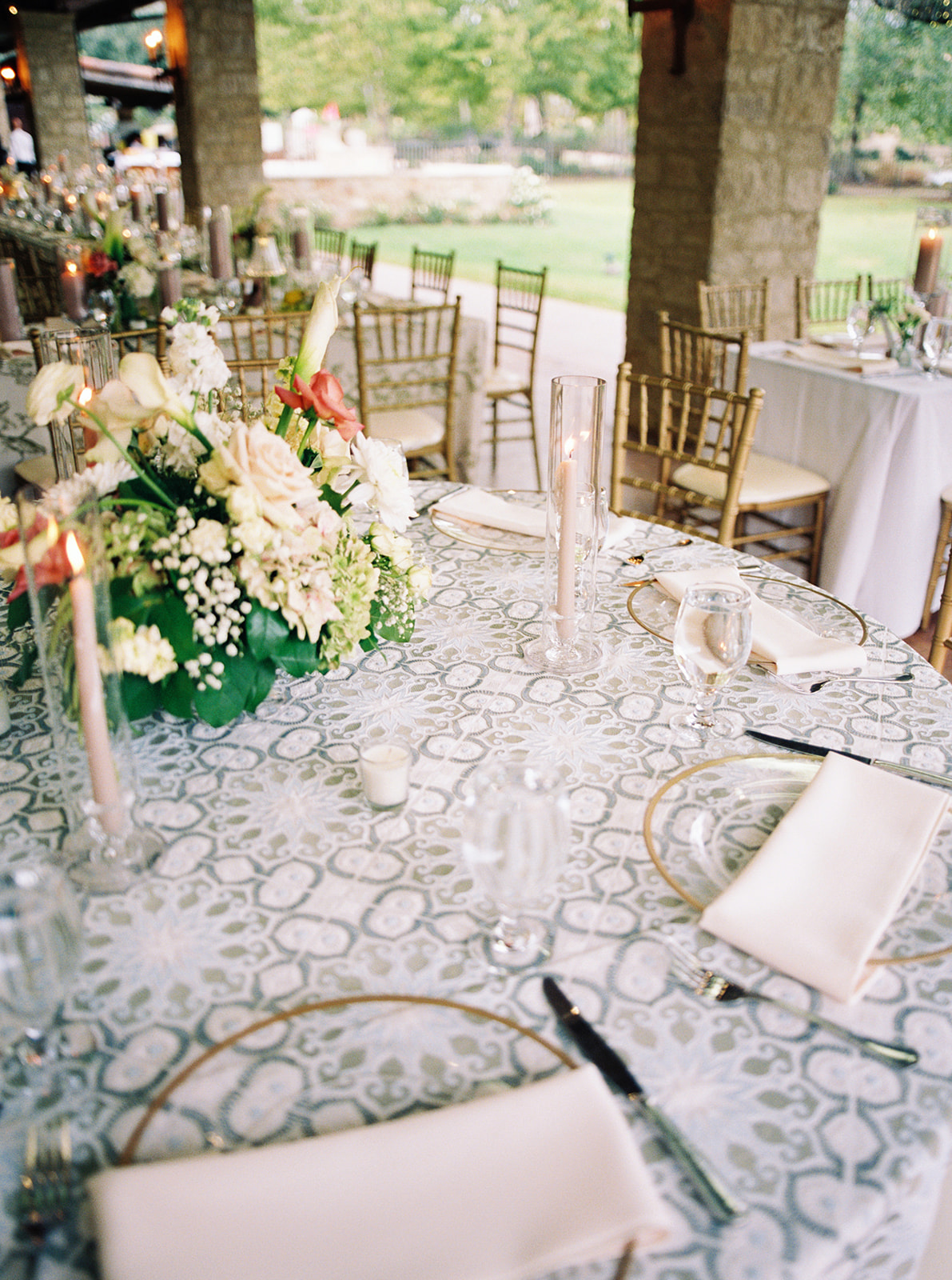 Elegant wedding reception setup with white and gold decor, floral arrangements, and a stone fireplace. Tables are set with white cloths and gold chairs under a draped ceiling at the houston oaks country club