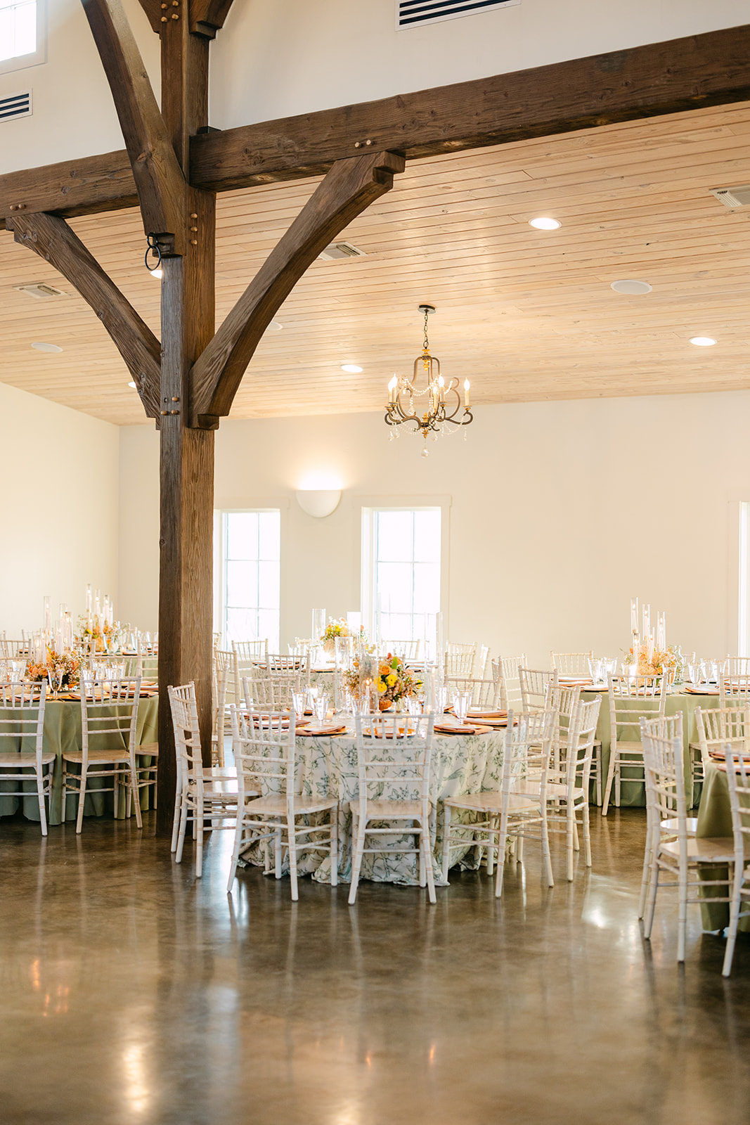 Elegant table setting with a floral centerpiece, surrounded by candles, glasses, and place settings with menus on gold chargers. White chairs encircle the table.