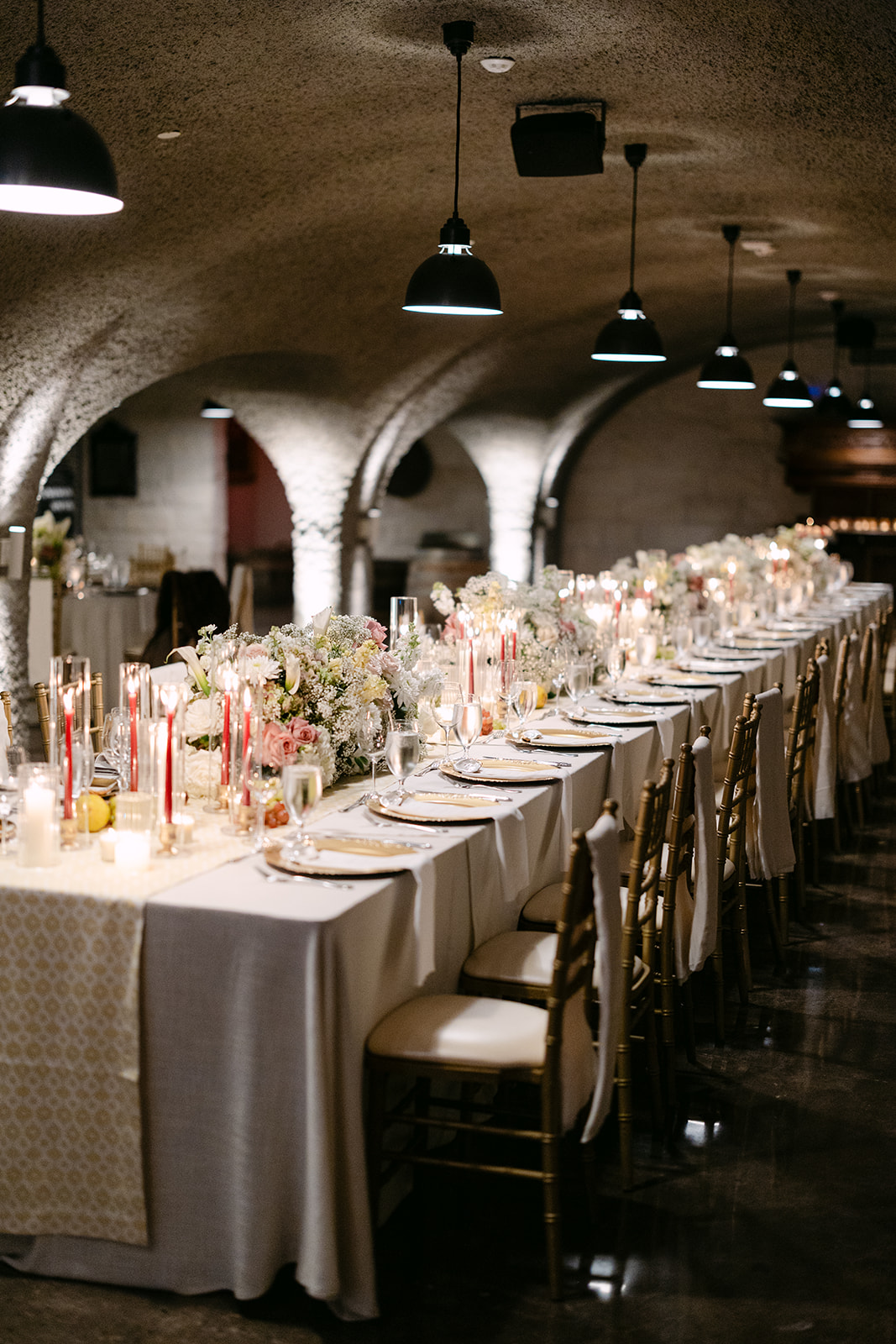 Elegant dining table set in a dimly lit room with curved arches, adorned with floral centerpieces, red candles, and elegant tableware.