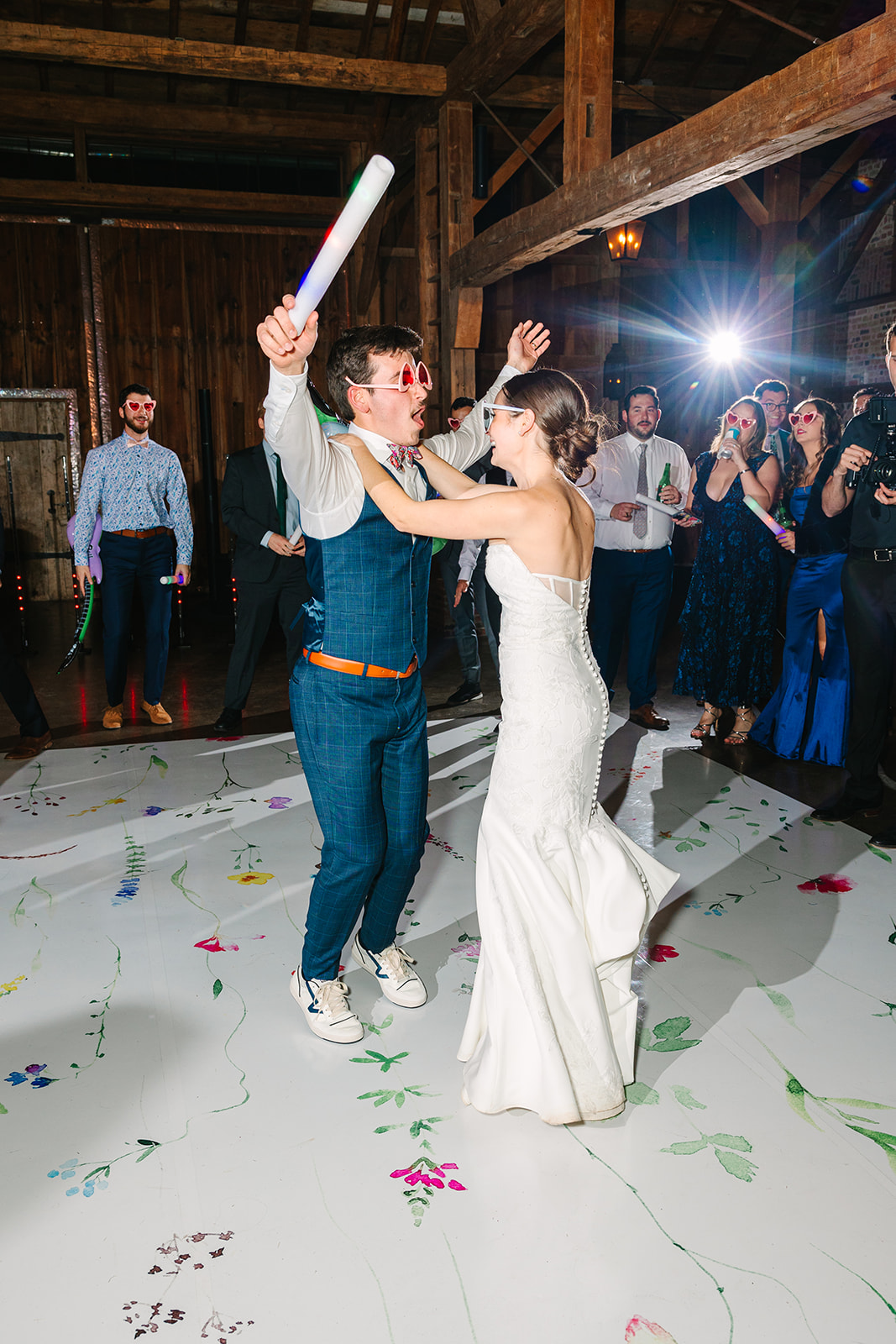 A group of people dressed formally dance and sing with inflatable microphones and glow sticks at a lively wedding at Beckendorff Farms in Katy, TX