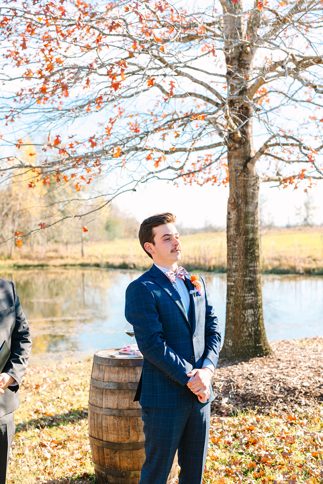 A bride and groom stand facing each other outdoors by a pond, holding hands during their wedding ceremony at Beckendorff Farms in Katy, TX