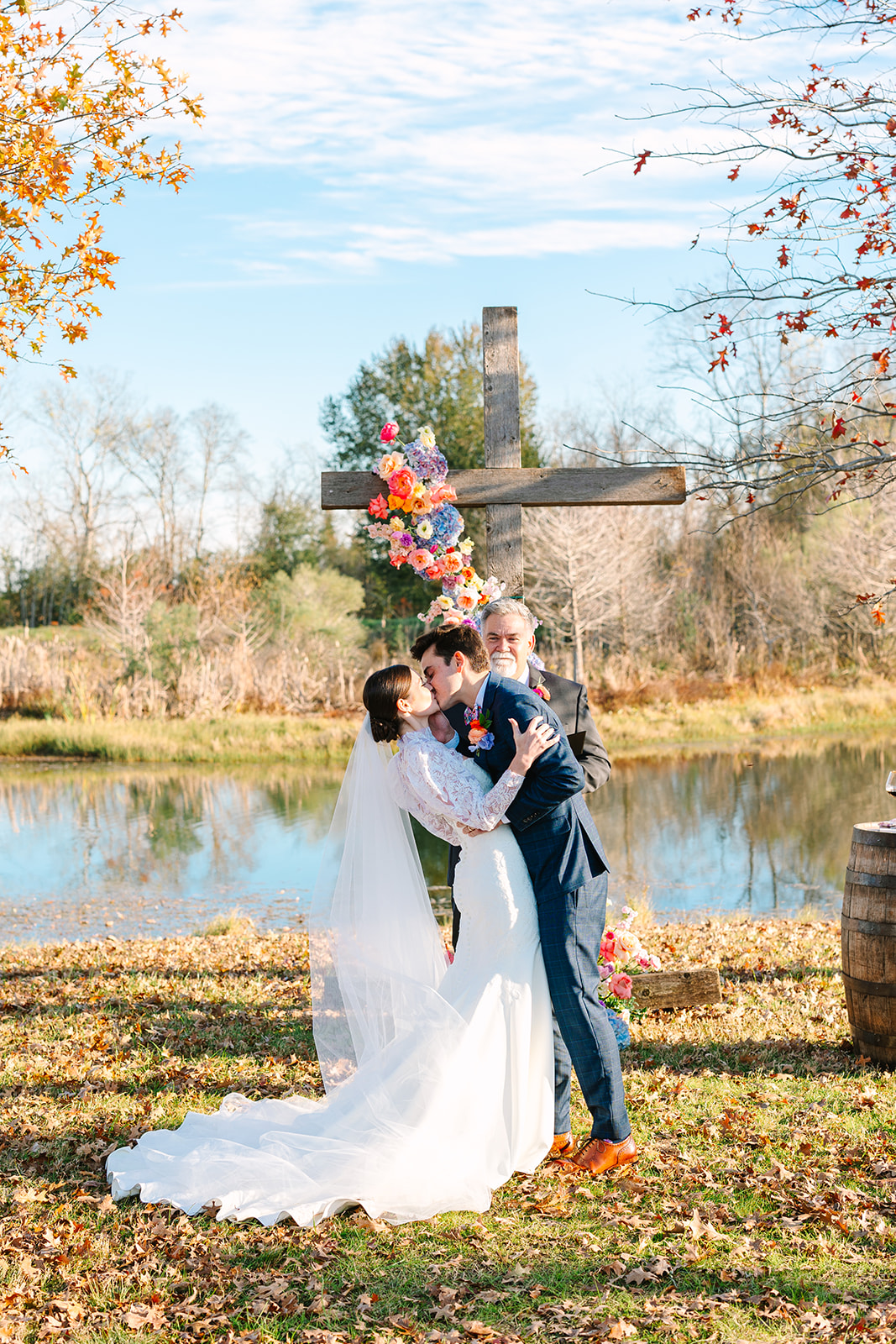 A bride and groom stand facing each other outdoors by a pond, holding hands during their wedding ceremony at Beckendorff Farms in Katy, TX