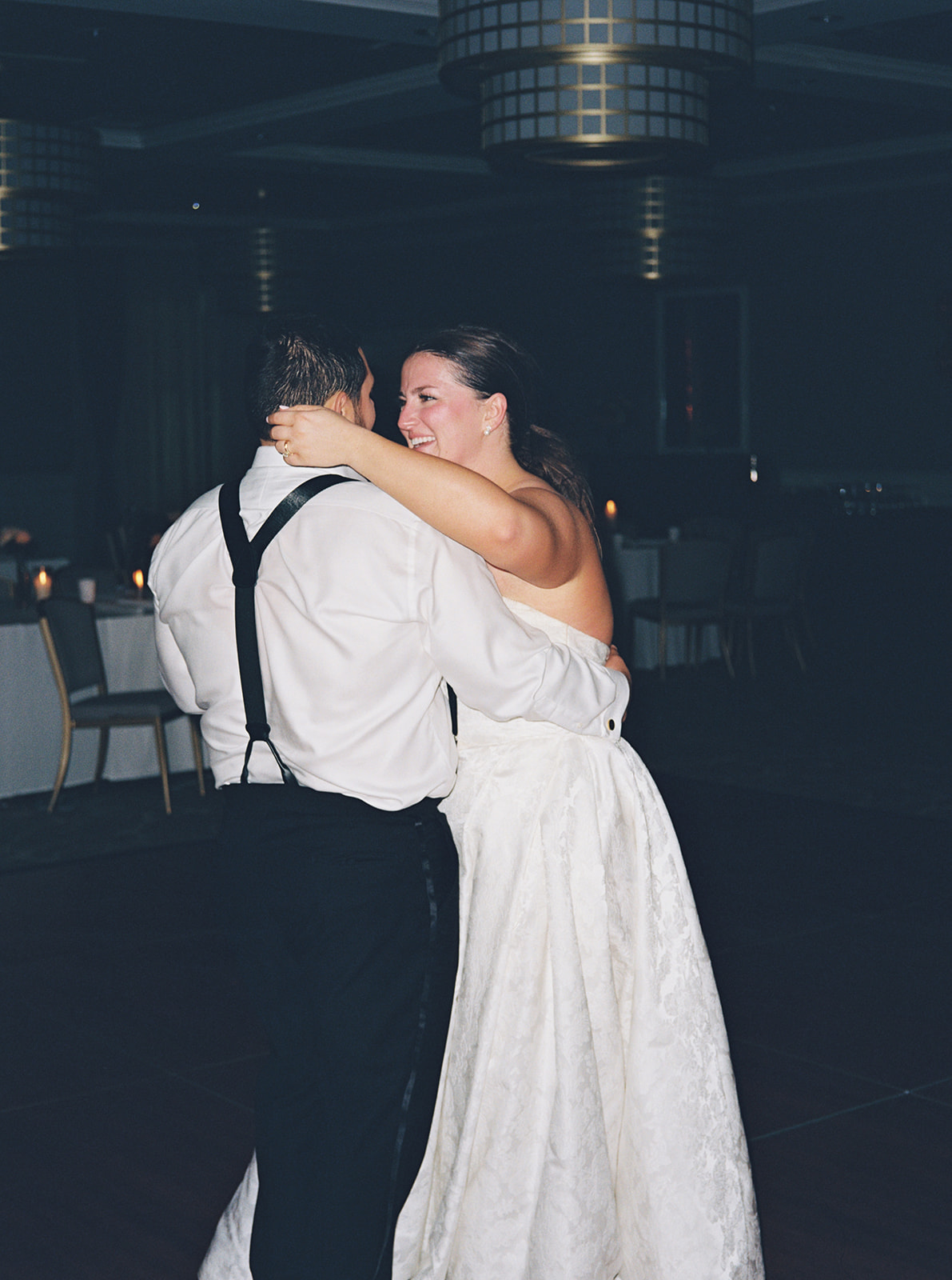A bride and groom dance together on a wooden floor while a live band performs in the background at their wedding reception.