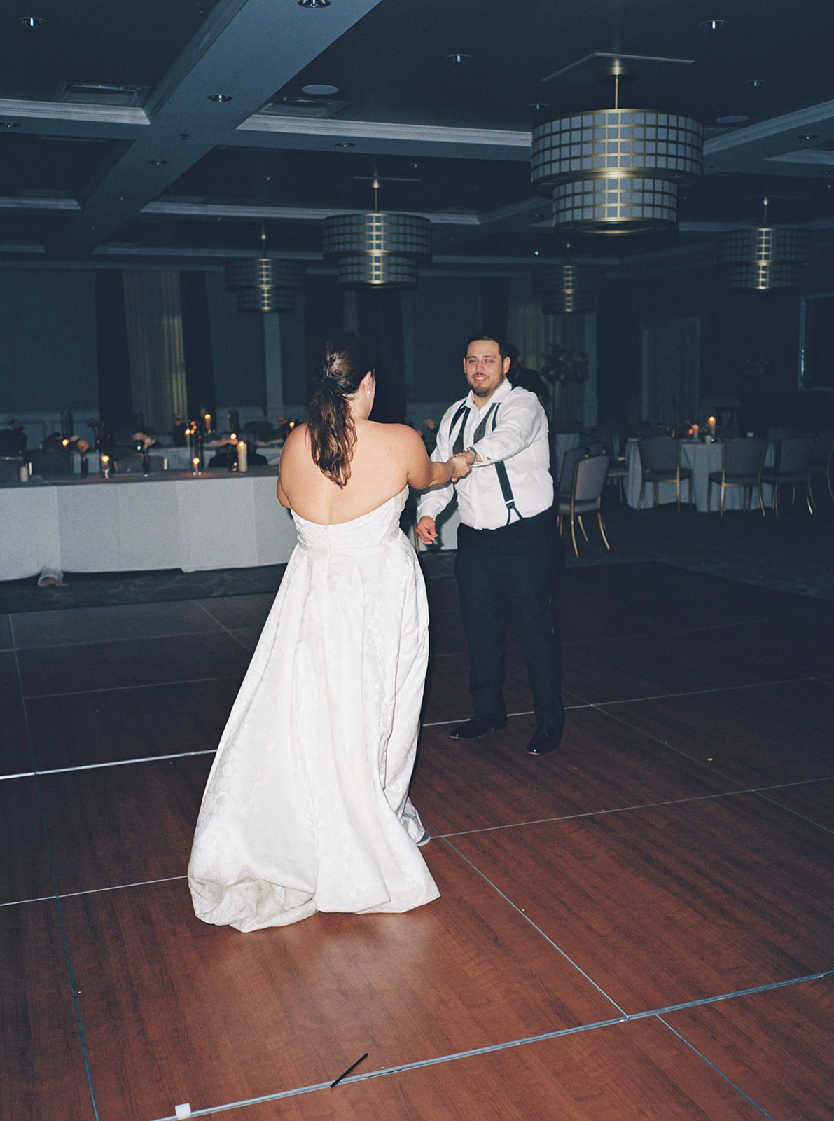 A bride and groom dance together on a wooden floor while a live band performs in the background at their wedding reception.