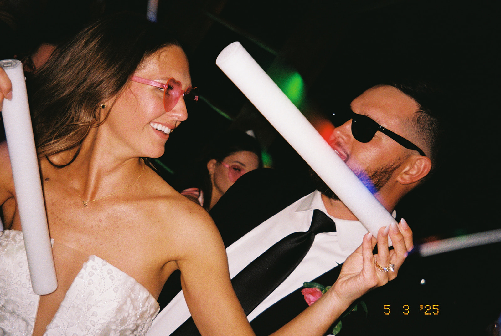 People dressed in semi-formal attire dance indoors holding light sticks. 