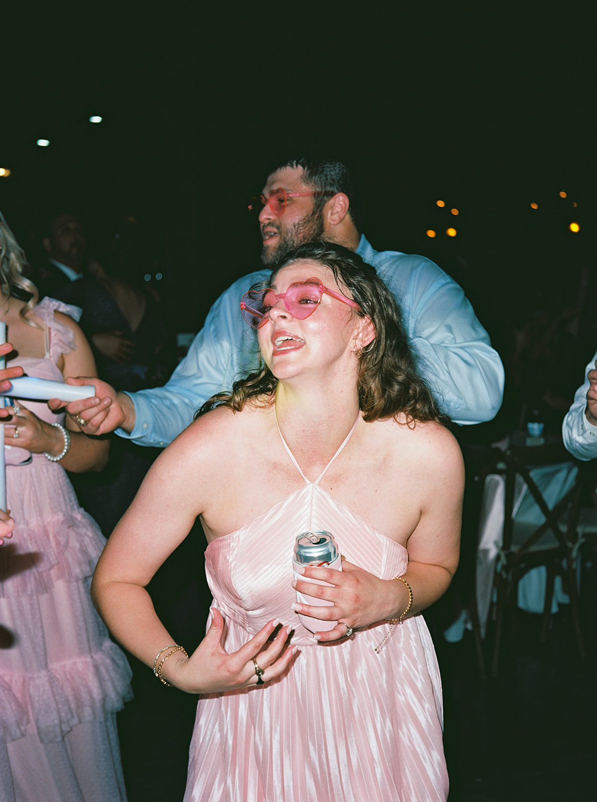 People dressed in semi-formal attire dance indoors holding light sticks. 