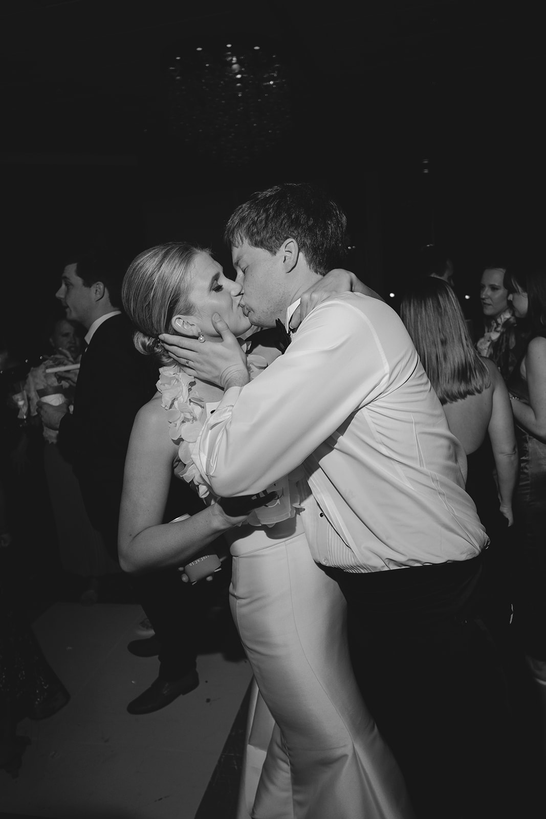 A couple dressed in formal attire kisses passionately on a crowded dance floor at an event or celebration.