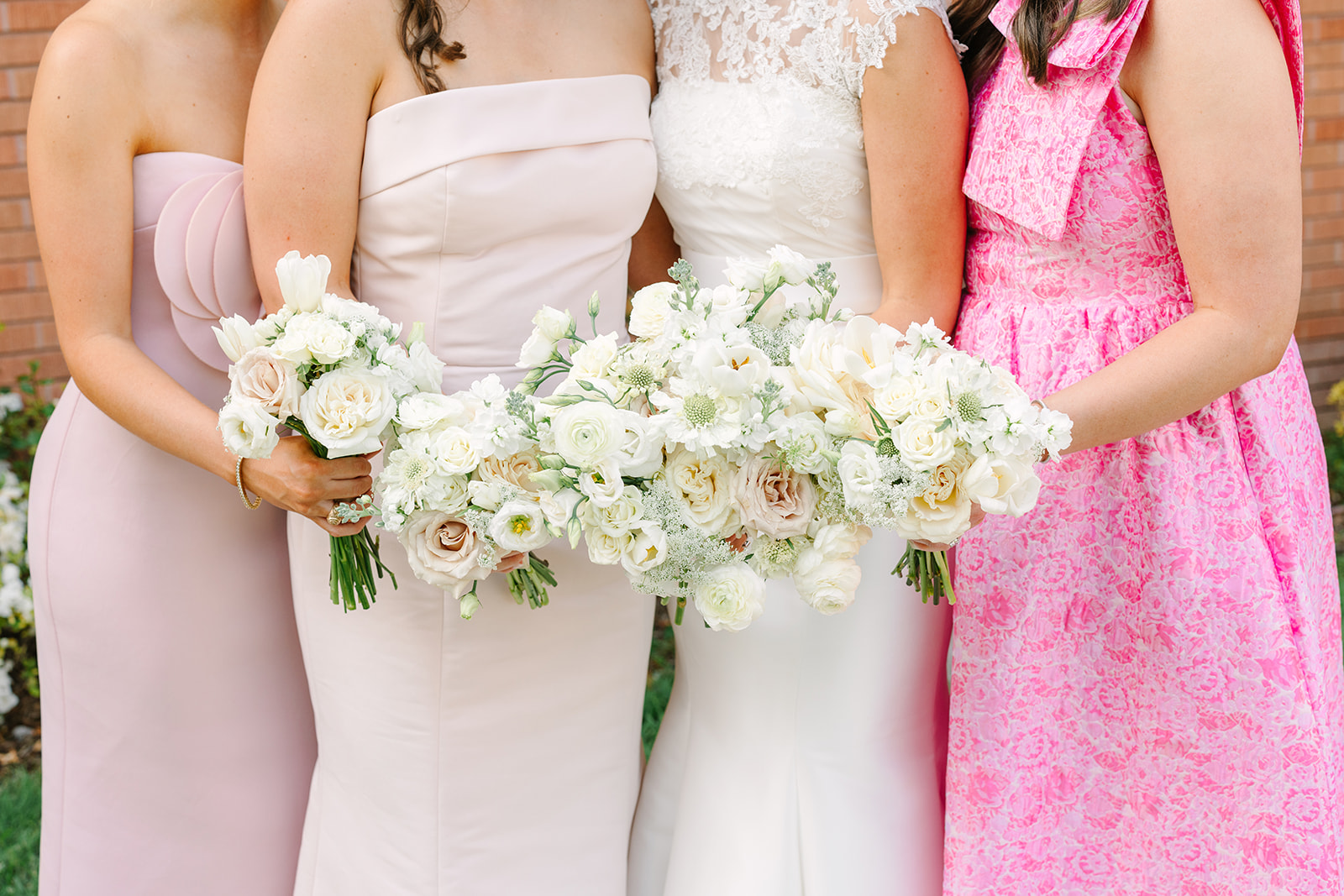 A wedding party of four women and four men stands in a line outdoors, dressed in formal attire, in front of a brick building for a Braeburn Country Club Houston Wedding