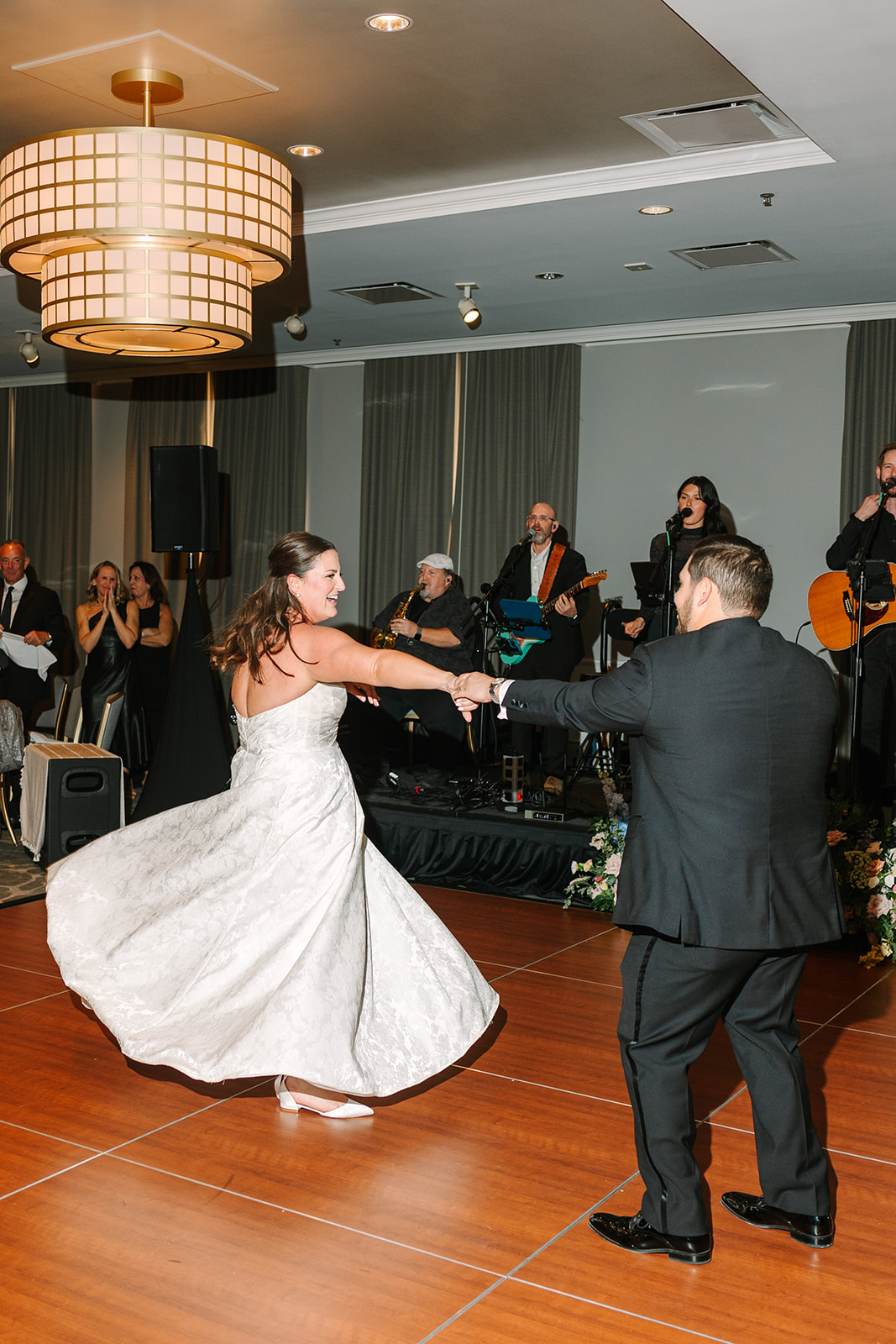 A bride and groom dance together on a wooden floor while a live band performs in the background at their wedding reception.