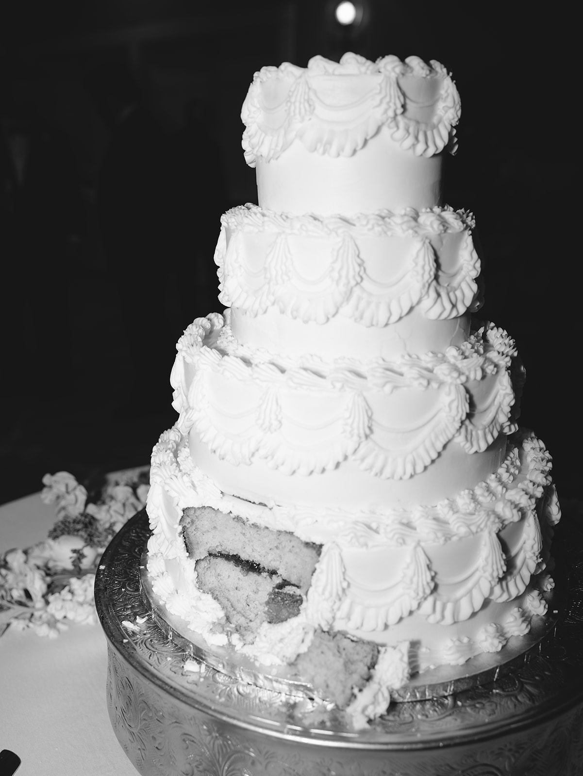 A bride and groom stand together, smiling, as they cut a large white wedding cake decorated with flowers at a reception.