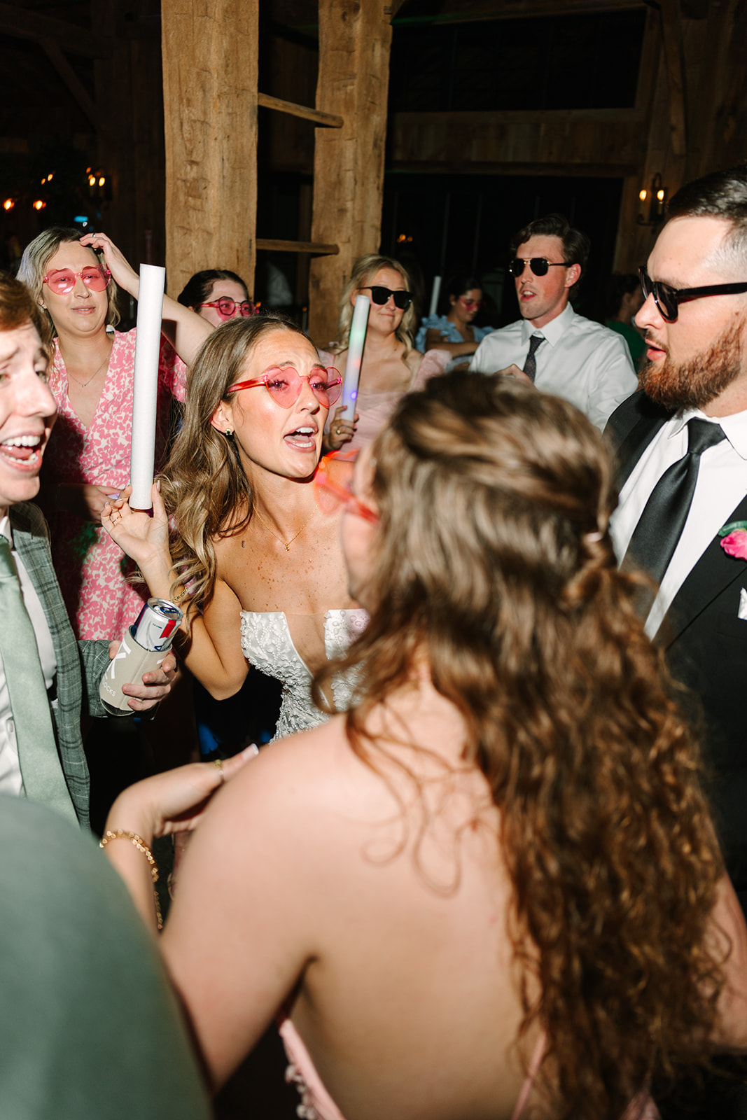 People dressed in semi-formal attire dance indoors holding light sticks. 