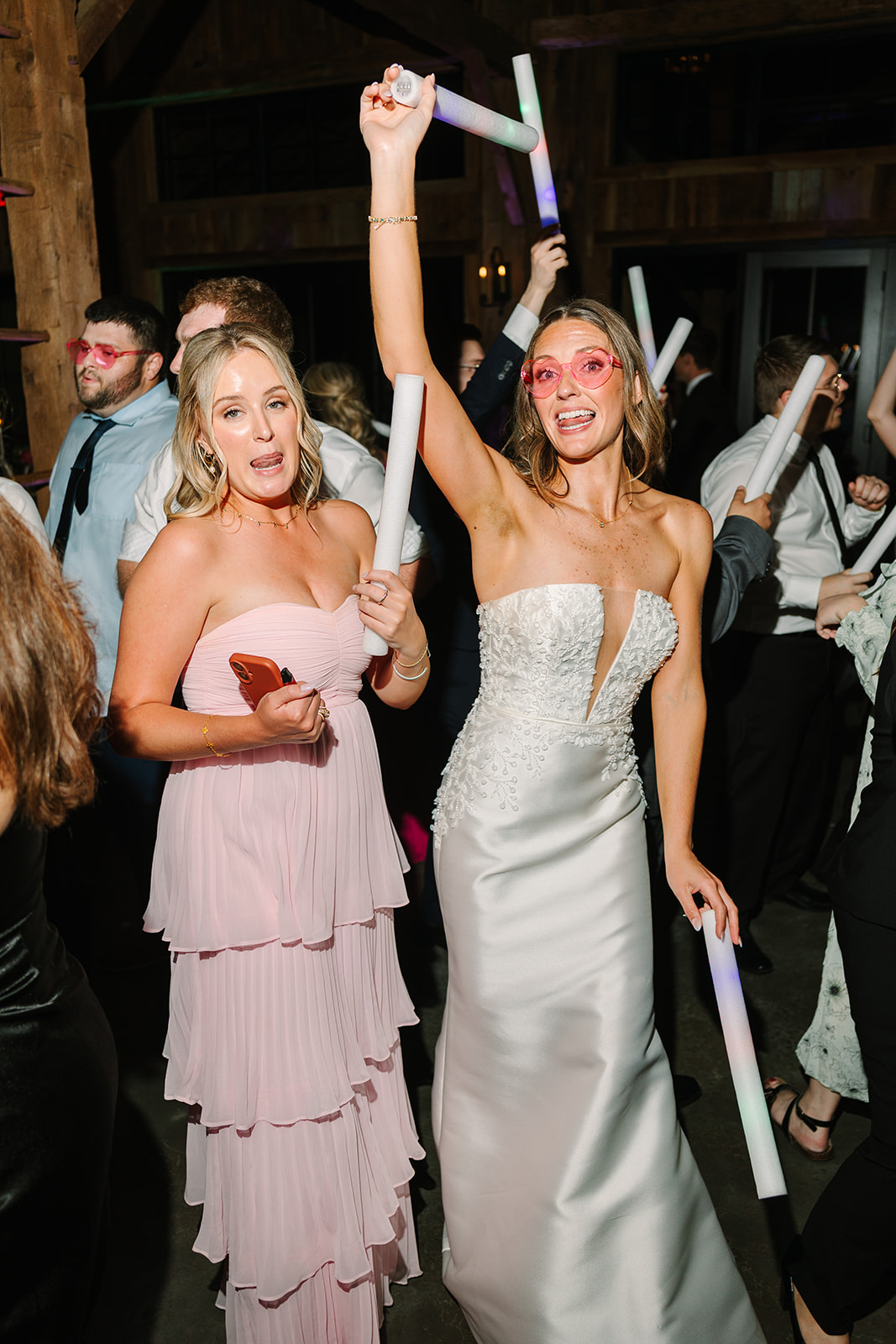 People dressed in semi-formal attire dance indoors holding light sticks. 