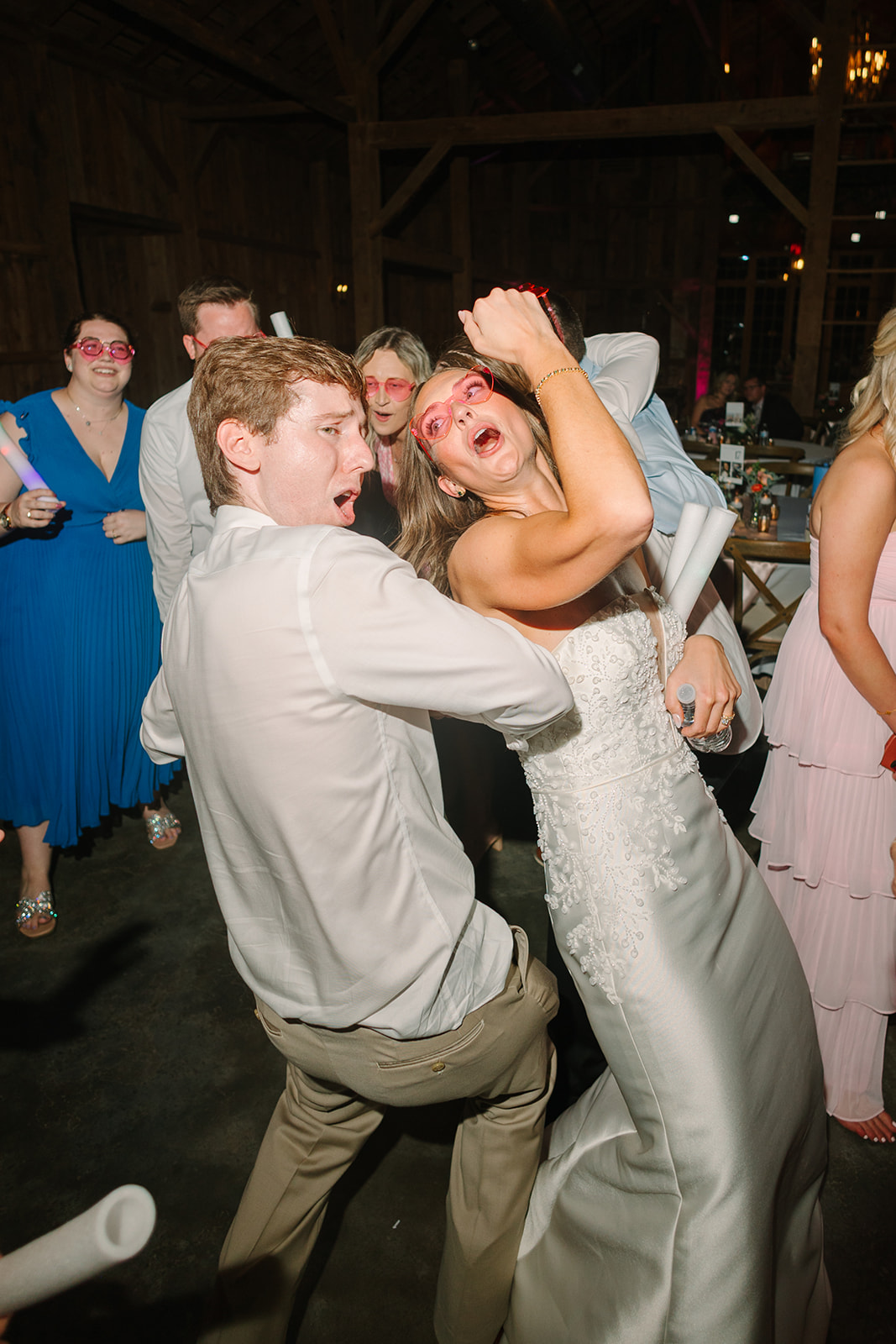 People dressed in semi-formal attire dance indoors holding light sticks. 