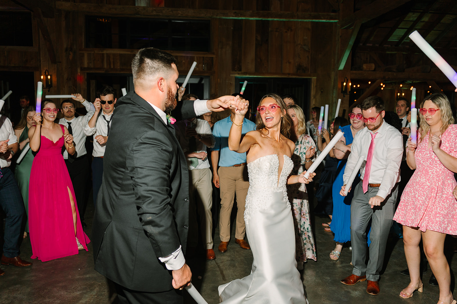 People dressed in semi-formal attire dance indoors holding light sticks. 