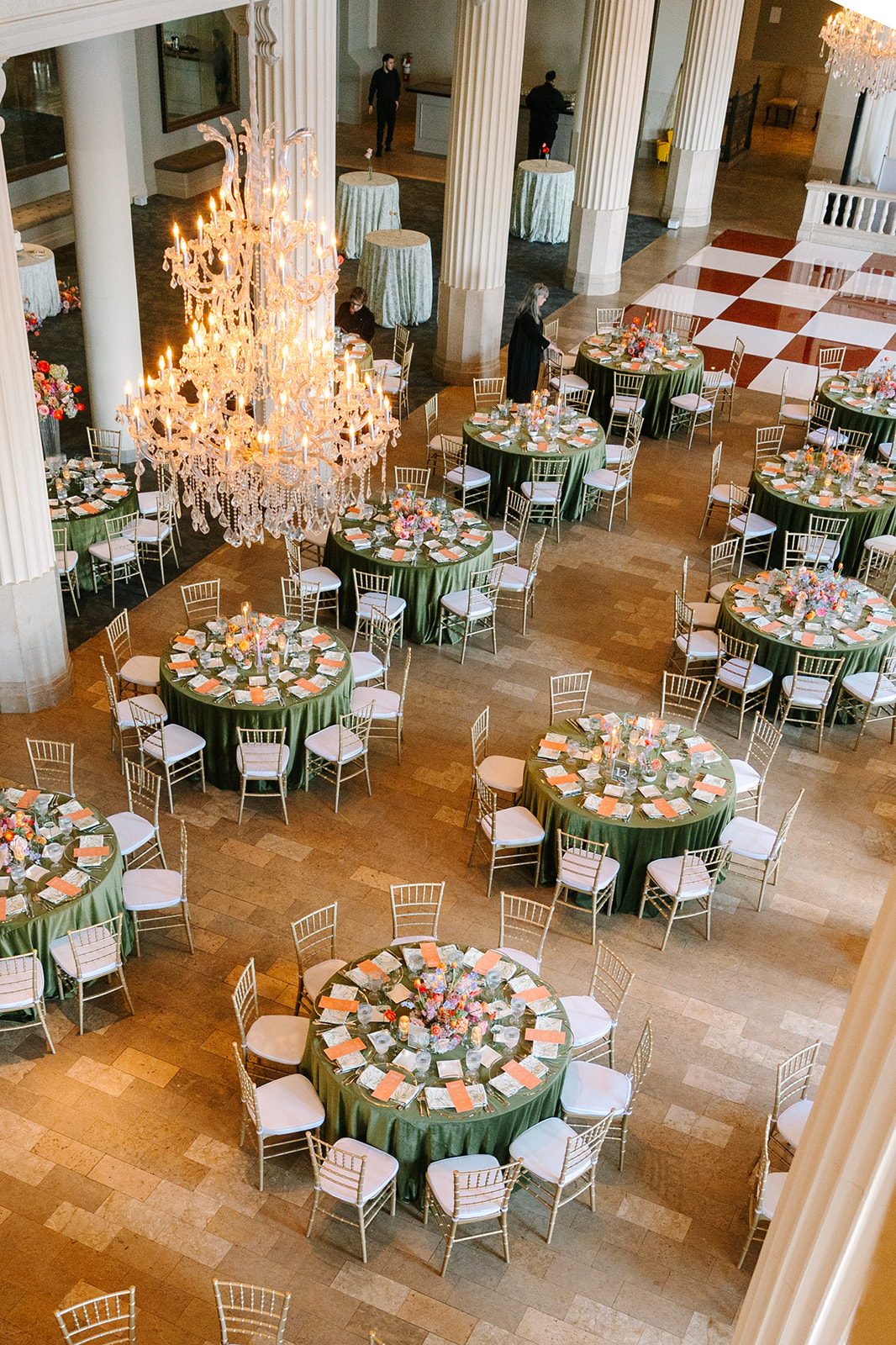 A formal banquet hall with round tables covered in green tablecloths, set for dining, white chairs, a large chandelier, and checkered flooring in the background at the corinthian houston