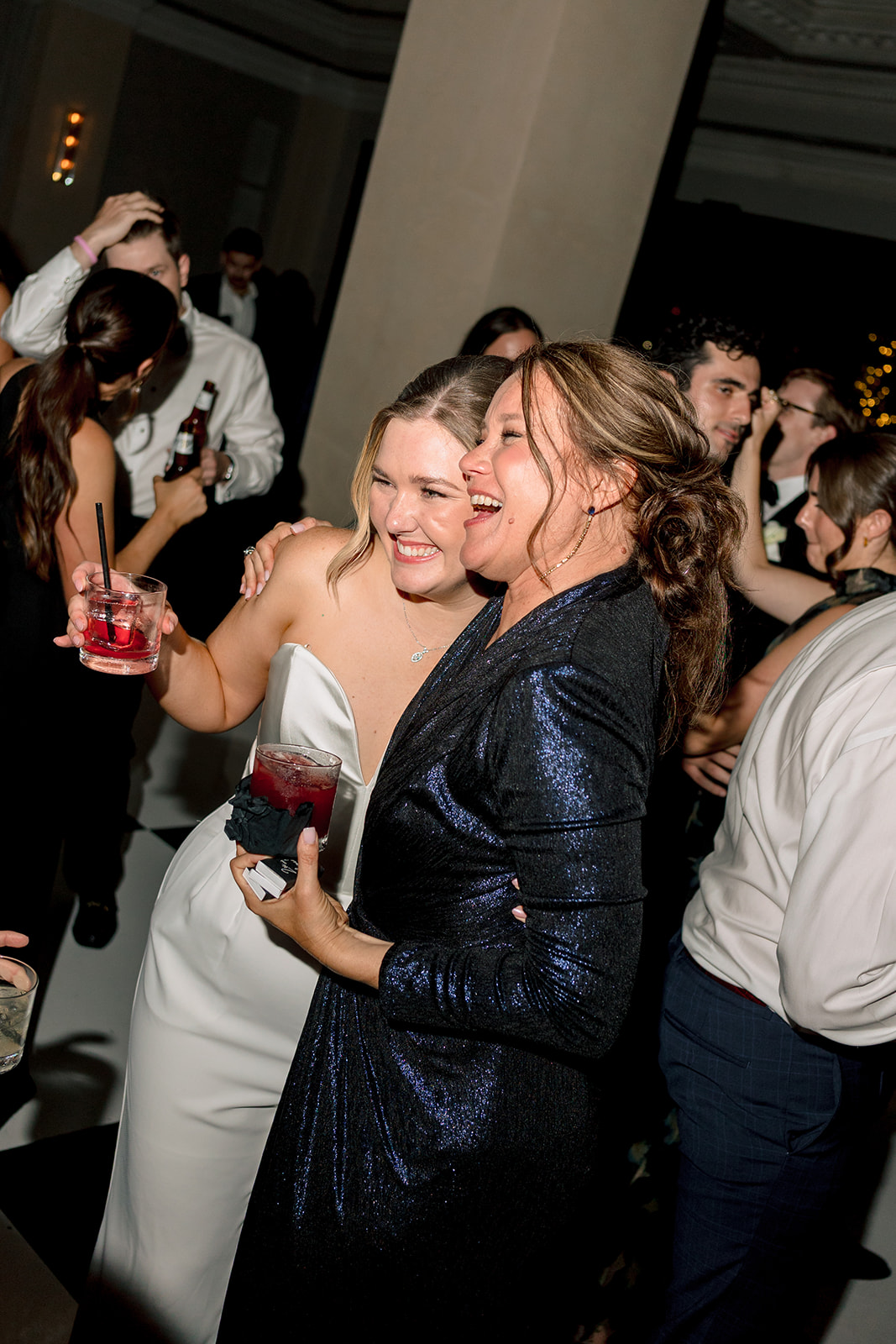 A group of people in formal attire and white hats laugh and dance together at a wedding at Le Tesserae 