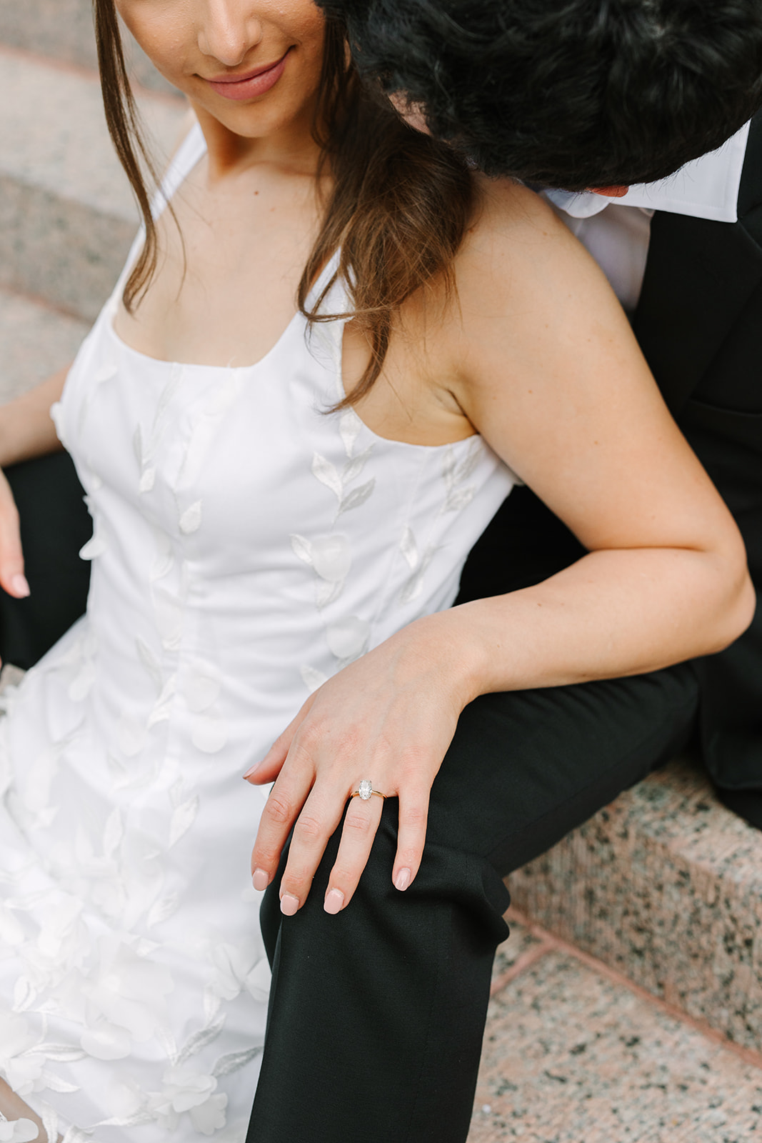 A man in a black suit and a woman in a white dress stand together outdoors on stone steps for their Downtown Houston Engagement Photos 