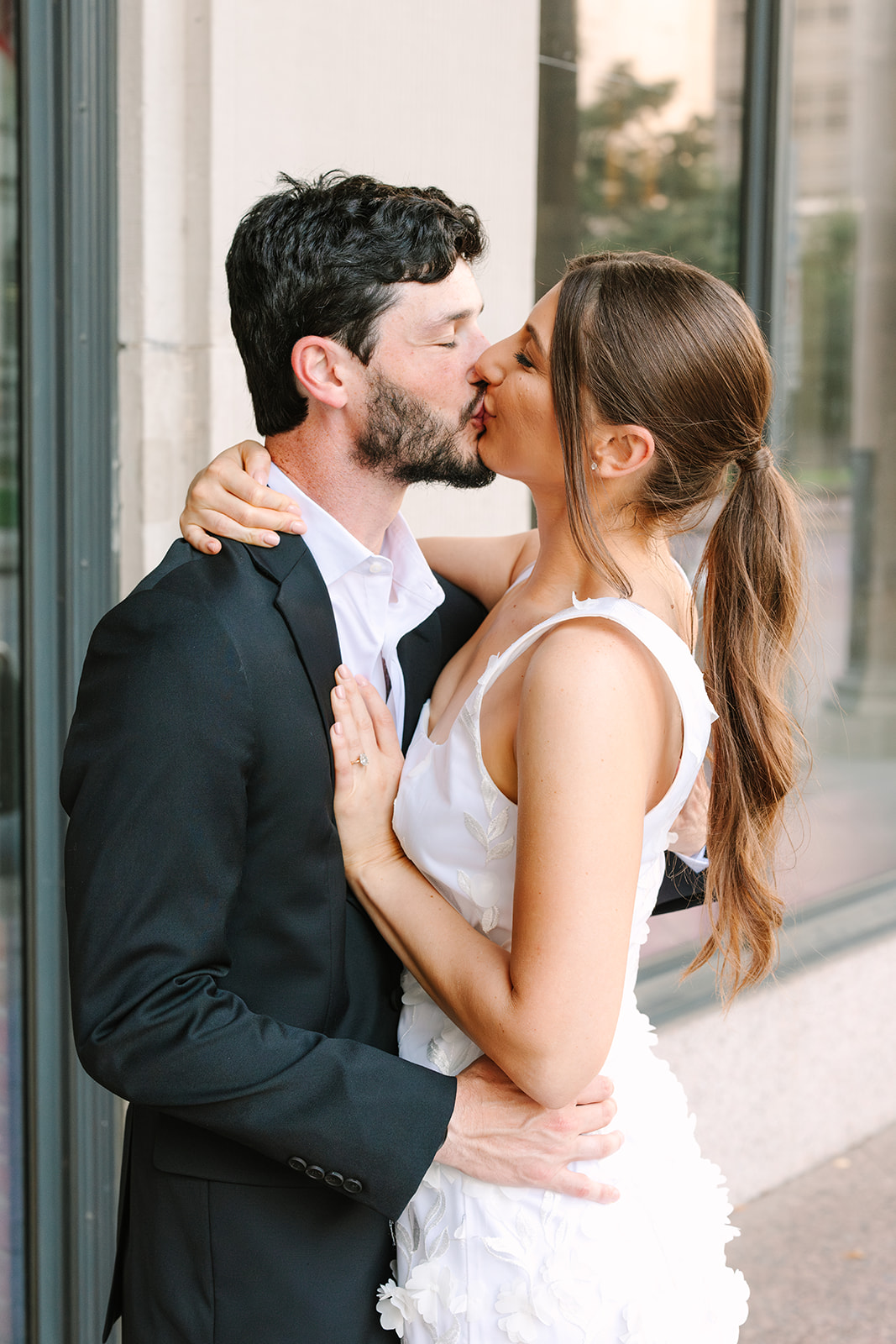 A couple dressed in wedding attire stand close together on a city sidewalk, smiling and laughing. The image is in black and white for Downtown Houston Engagement Photos