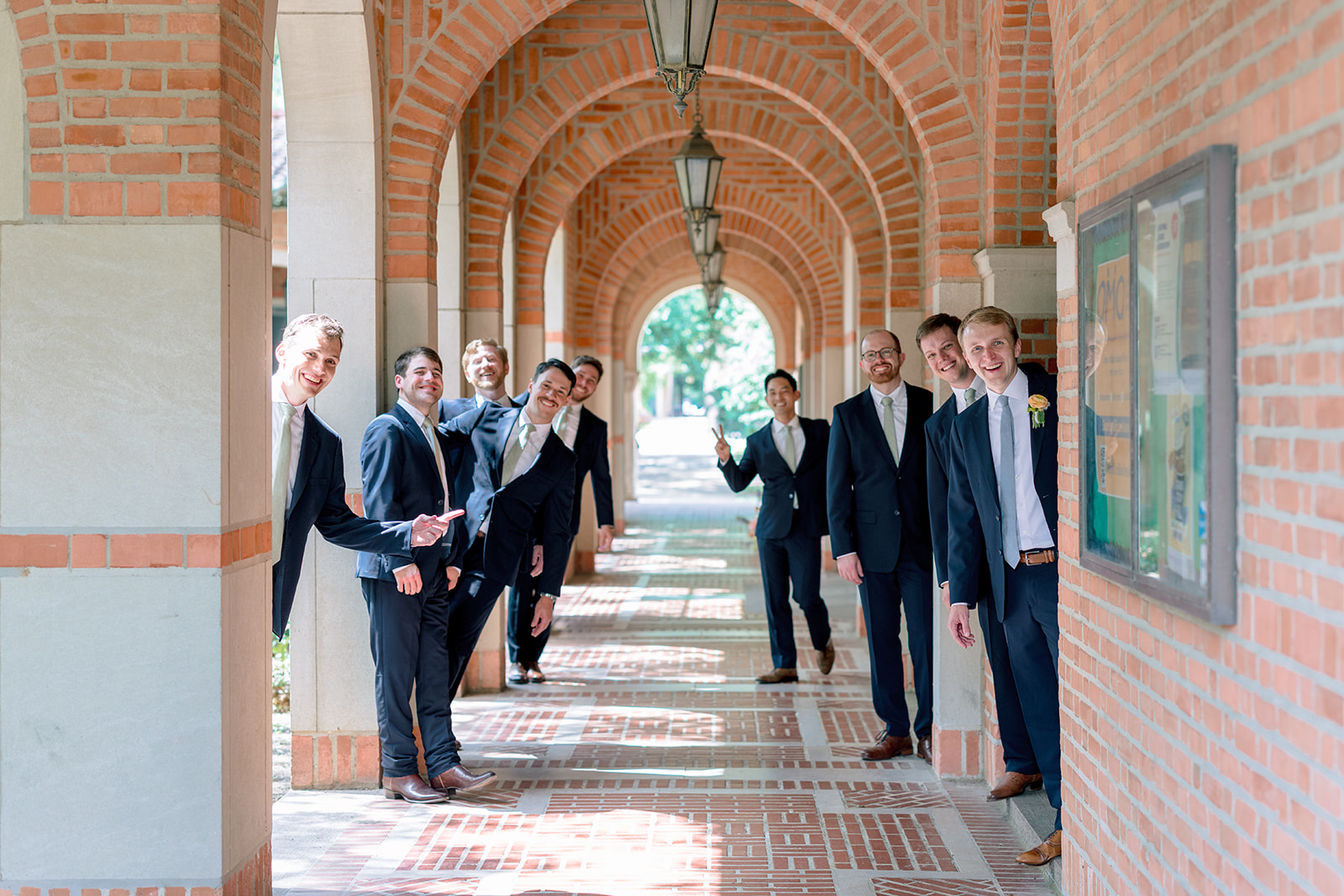 A wedding party poses outdoors in front of a building with arches, with bridesmaids in colorful dresses and groomsmen in dark suits at the garden wedding venue