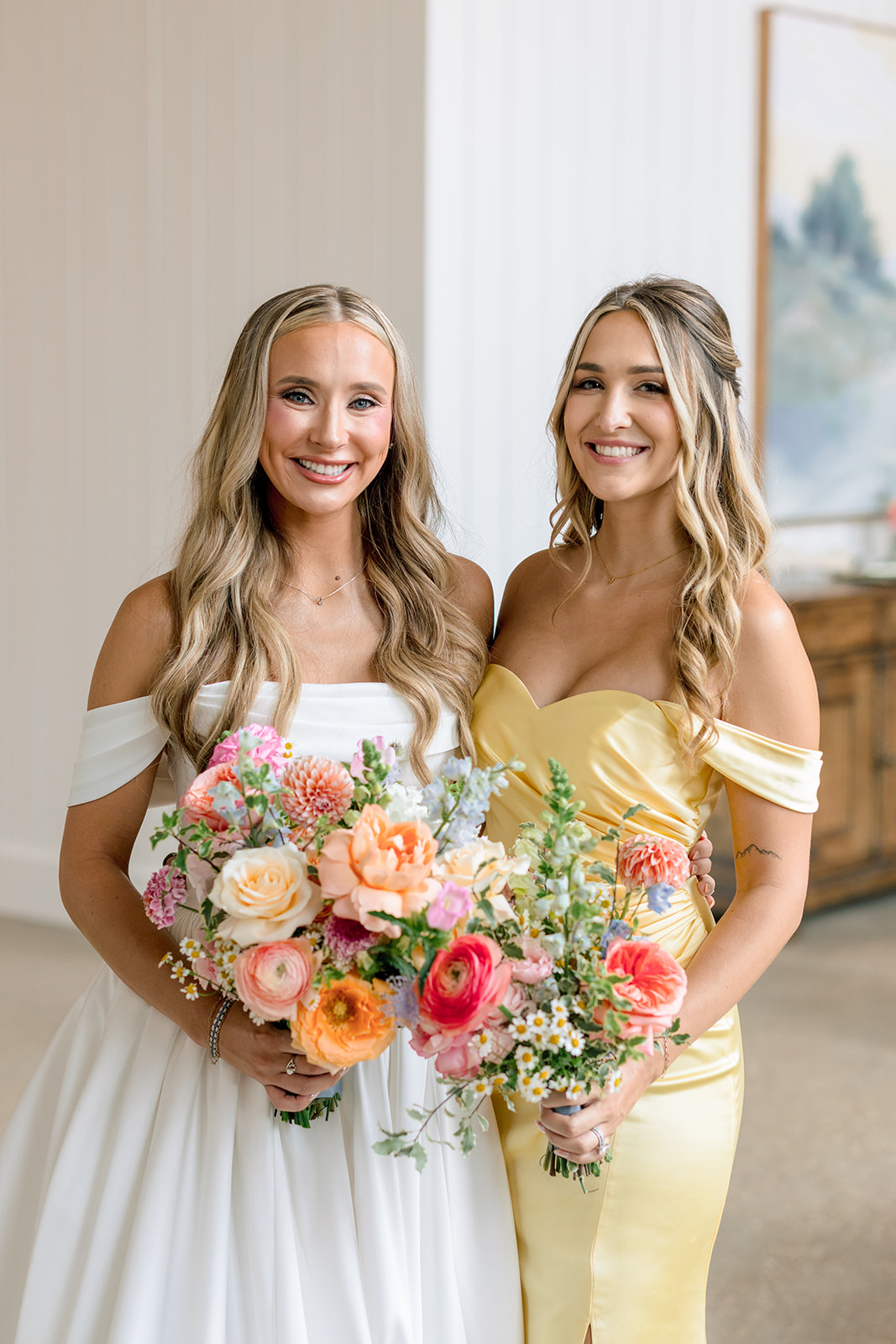A bride in a white dress stands with her bridesmaids, who are wearing long dresses in various pastel colors and holding bouquets of flowers at the blue magnolia
