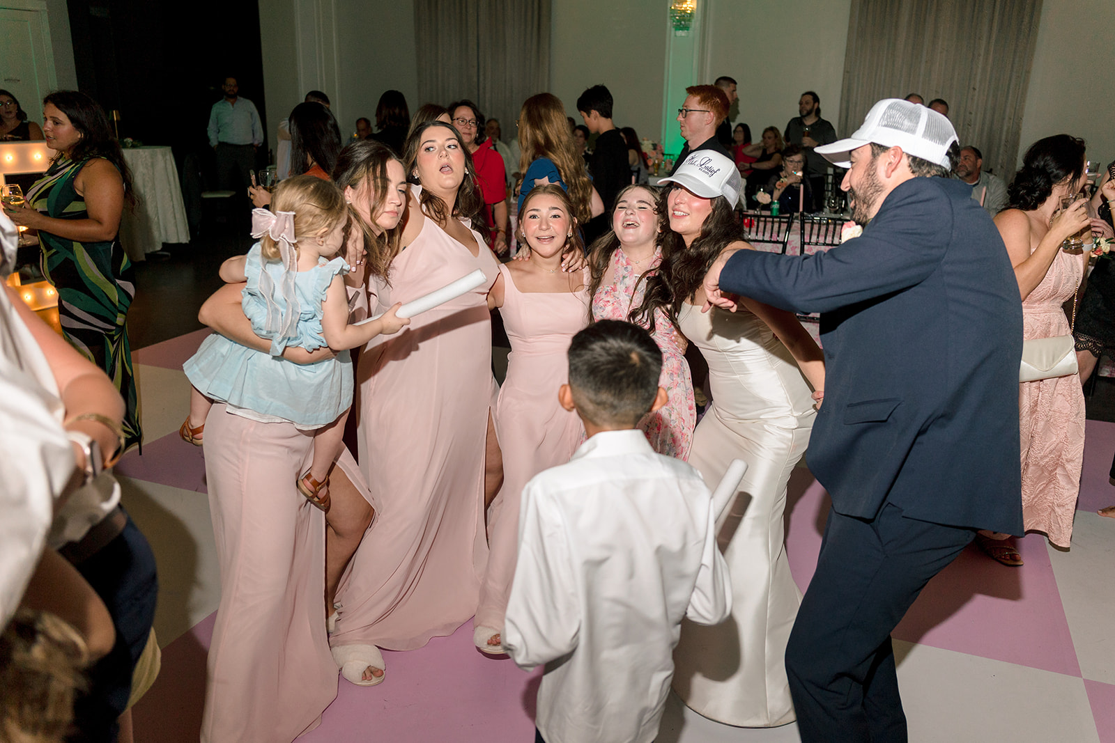 a group of people dance on a pink checkered floor at a celebration