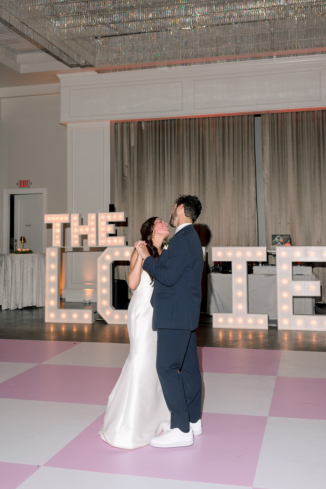 A bride and groom walk outside at night, smiling and holding hands, while guests surround them holding lit sparklers.