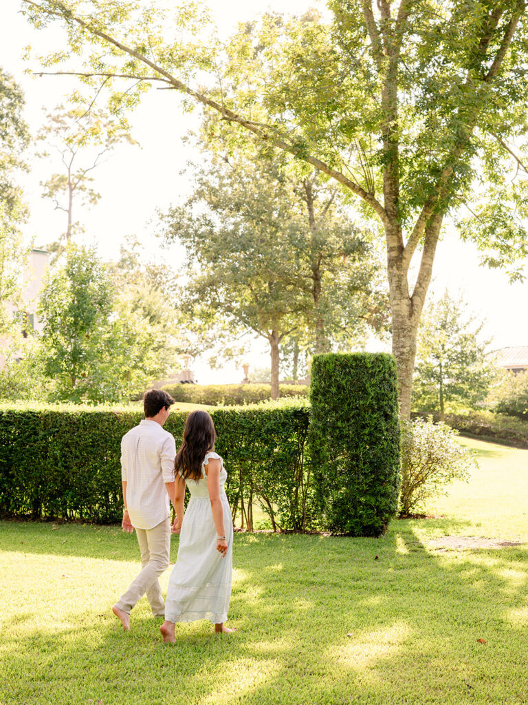 Couple walking away together across the sunlit lawn at Bayou Bend Gardens in Houston, TX